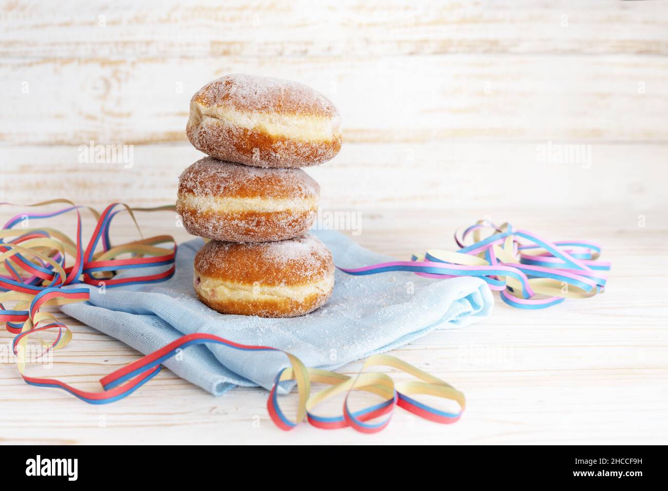 Stapel Berliner Donuts auch Krapfen genannt mit Partystreamer auf Serviette und einem leichten Holztisch, frittiertem Gebäck für Fasching und Neujahr Stockfoto