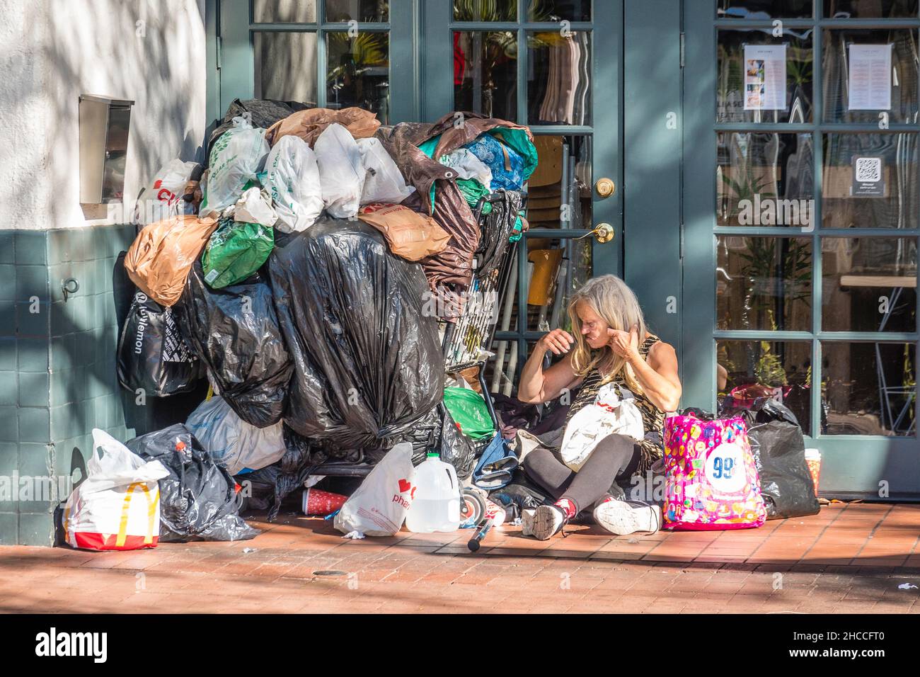 Eine chronisch obdachlose Frau und ihre weltlichen Besitztümer stapelten sich neben ihr vor einem geschlossenen Schaufenster. Stockfoto