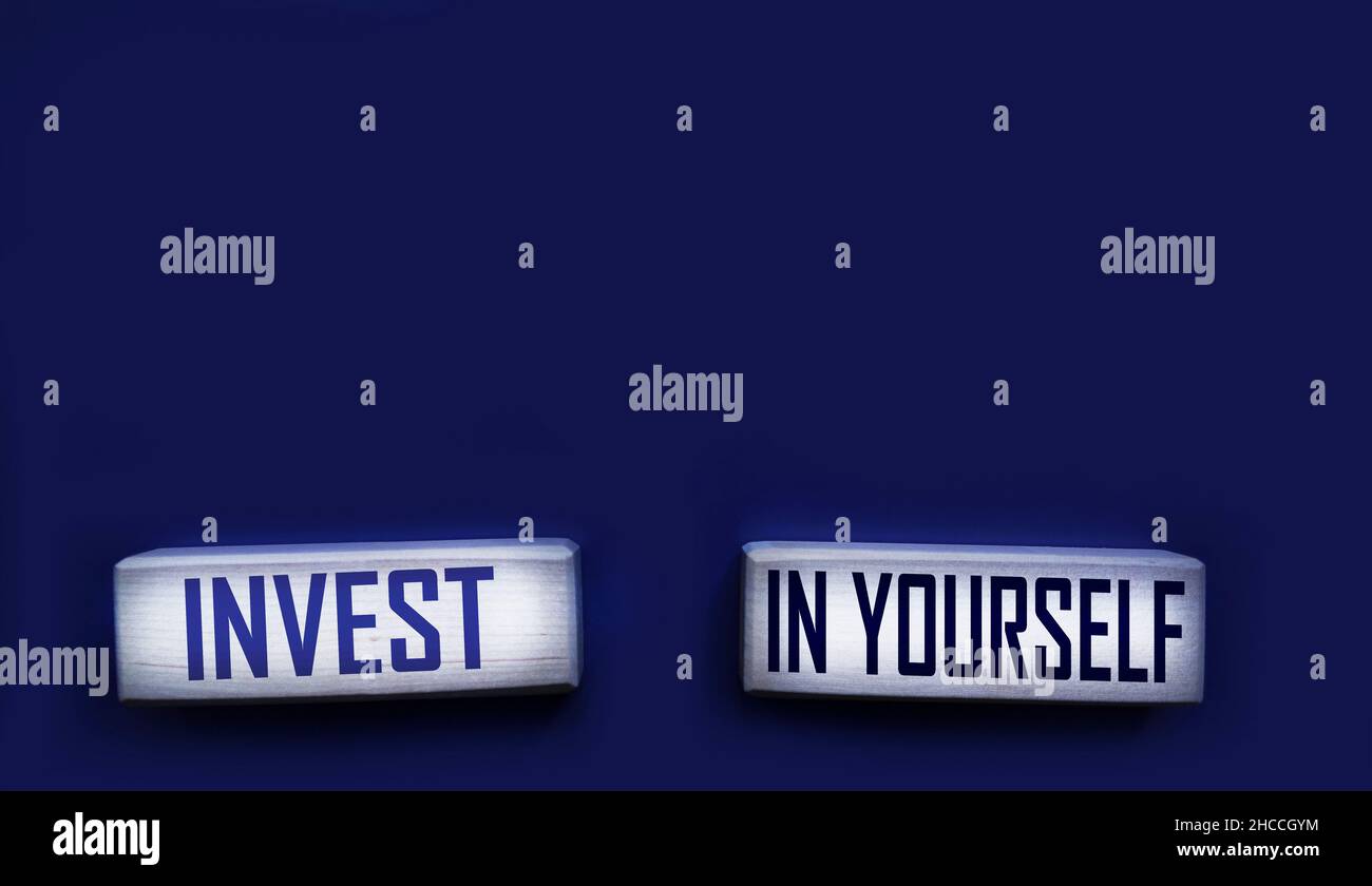 Investieren Sie in sich selbst. Motivierende Wörter in hölzernen Buchstaben auf blauem Hintergrund isoliert Stockfoto