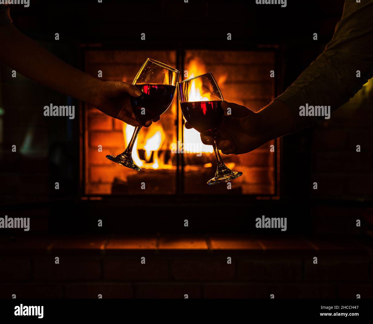 Nahaufnahme des Paares Hände klirende Gläser Wein in der Nähe des warmen Kamin im Haus Stockfoto