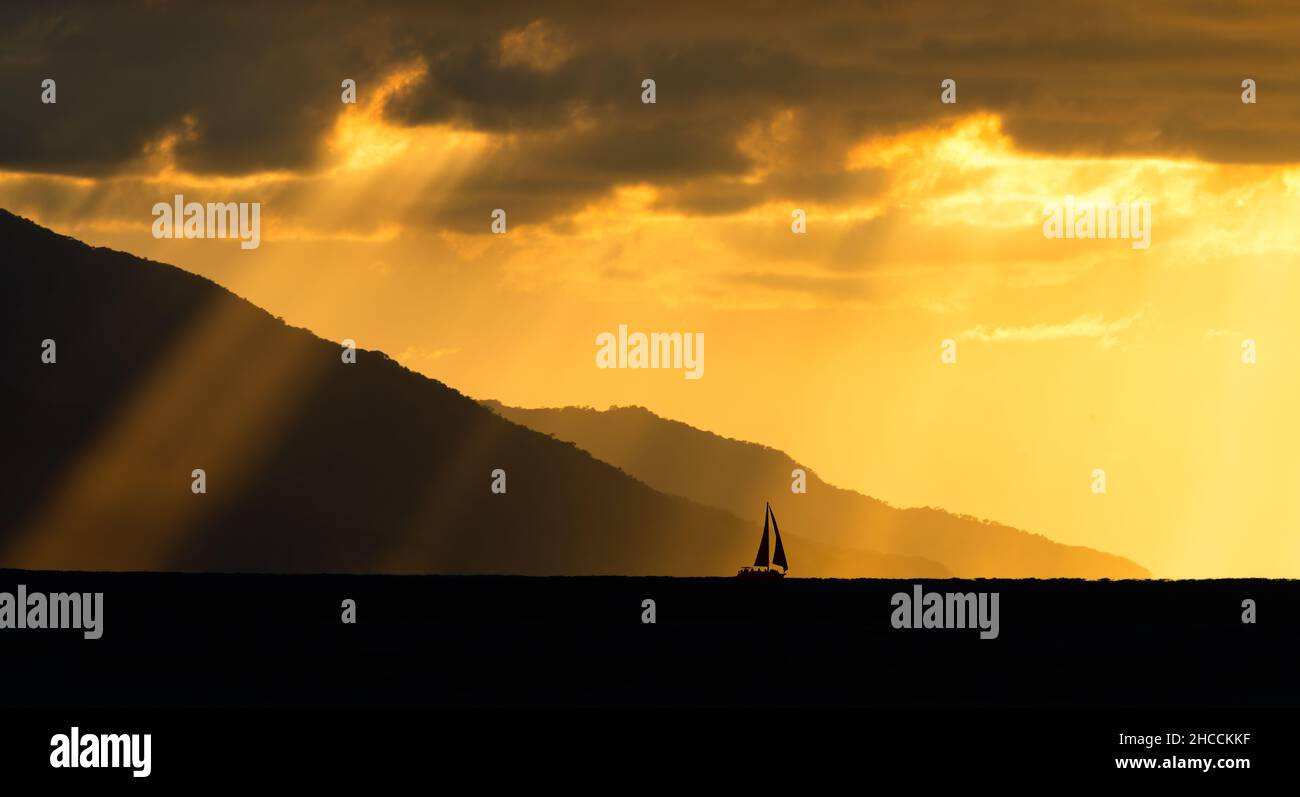 Sonnenstrahlen strahlen strahlen strahlen auf das Meer aus, während EIN Segelboot sailt Entlang Des Ozeanhorizonts Stockfoto