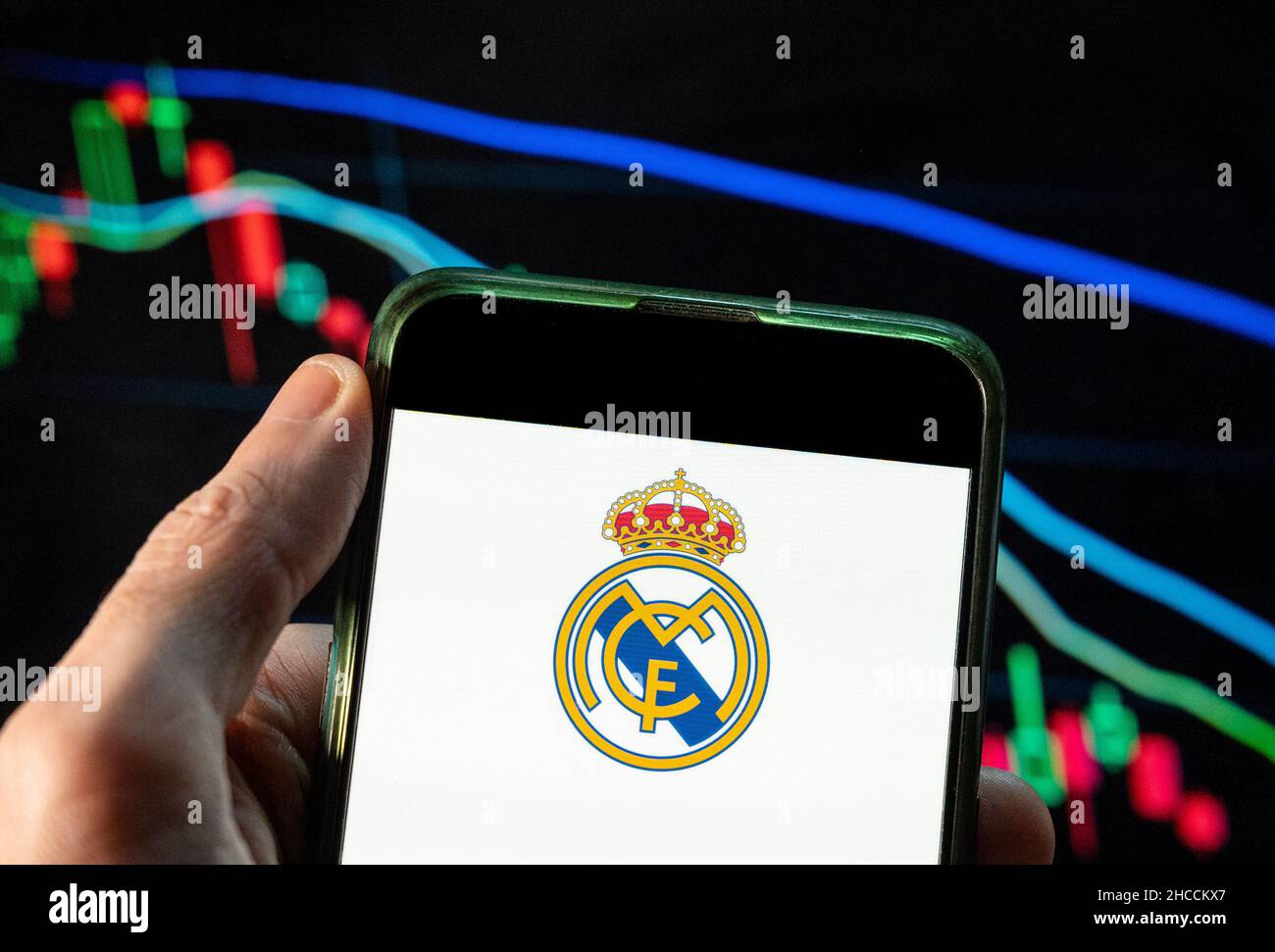 China. 09th Dez 2021. In dieser Abbildung sehen Sie das spanische Profi-Fußballteam Real Madrid Club de Fútbol, das gemeinhin als Real Madrid-Logo bekannt ist, das auf einem Smartphone mit einem Index der wirtschaftlichen Börse im Hintergrund angezeigt wird. (Foto von Budrul Chukrut/SOPA Images/Sipa USA) Quelle: SIPA USA/Alamy Live News Stockfoto