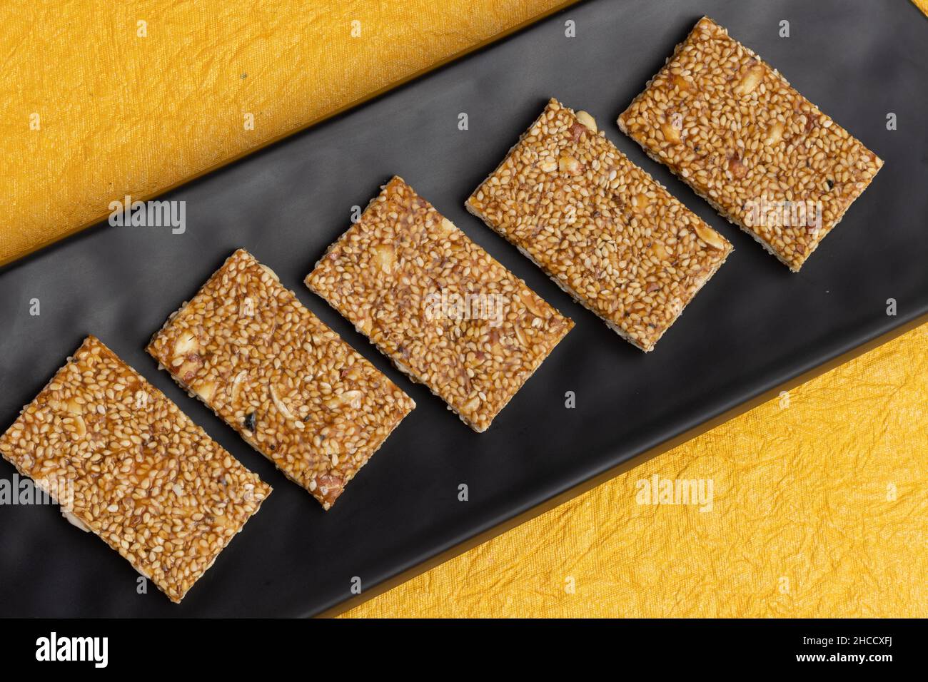 Traditionelle Süßigkeiten Mithai aus Indien isoliert auf gelbem Hintergrund für Makar Sankranti Lohri Gajak auch bekannt als Gur Gajjak Gazak Kachak Til Patti Stockfoto