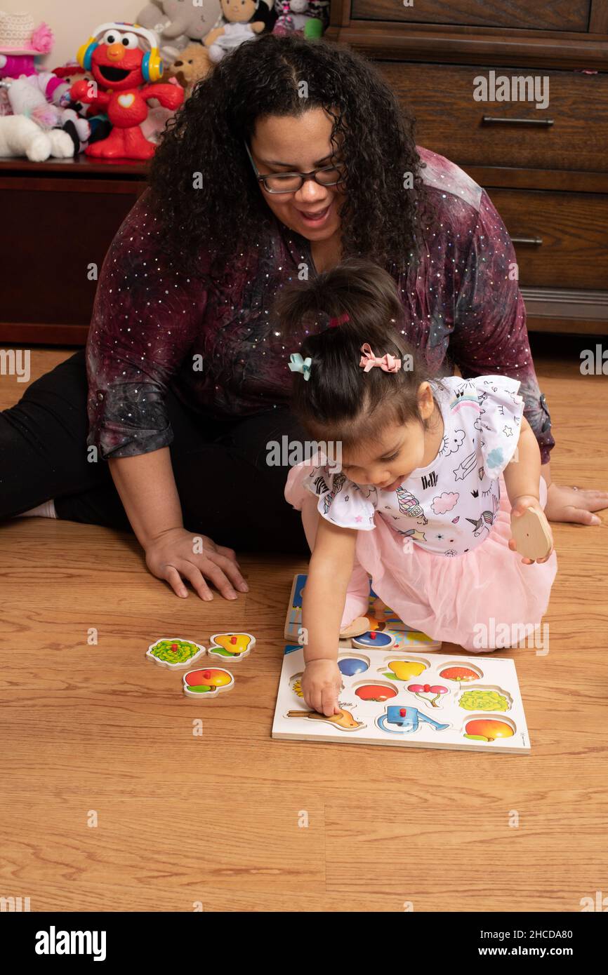 17 Monate altes Kleinkind Mädchen mit Mutter spielen mit Pflock Puzzle Stück Mutter hilft ihr, im Gespräch mit ihr Stockfoto