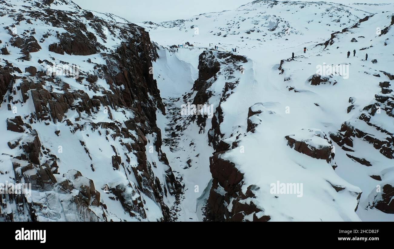 Luftaufnahme von steilen Felsen mit weißem Schnee durch das blaue Meer bedeckt, Schönheit der Winter Natur Konzept. Flug über die wunderschöne felsige Küste in der Wintersaison. Stockfoto