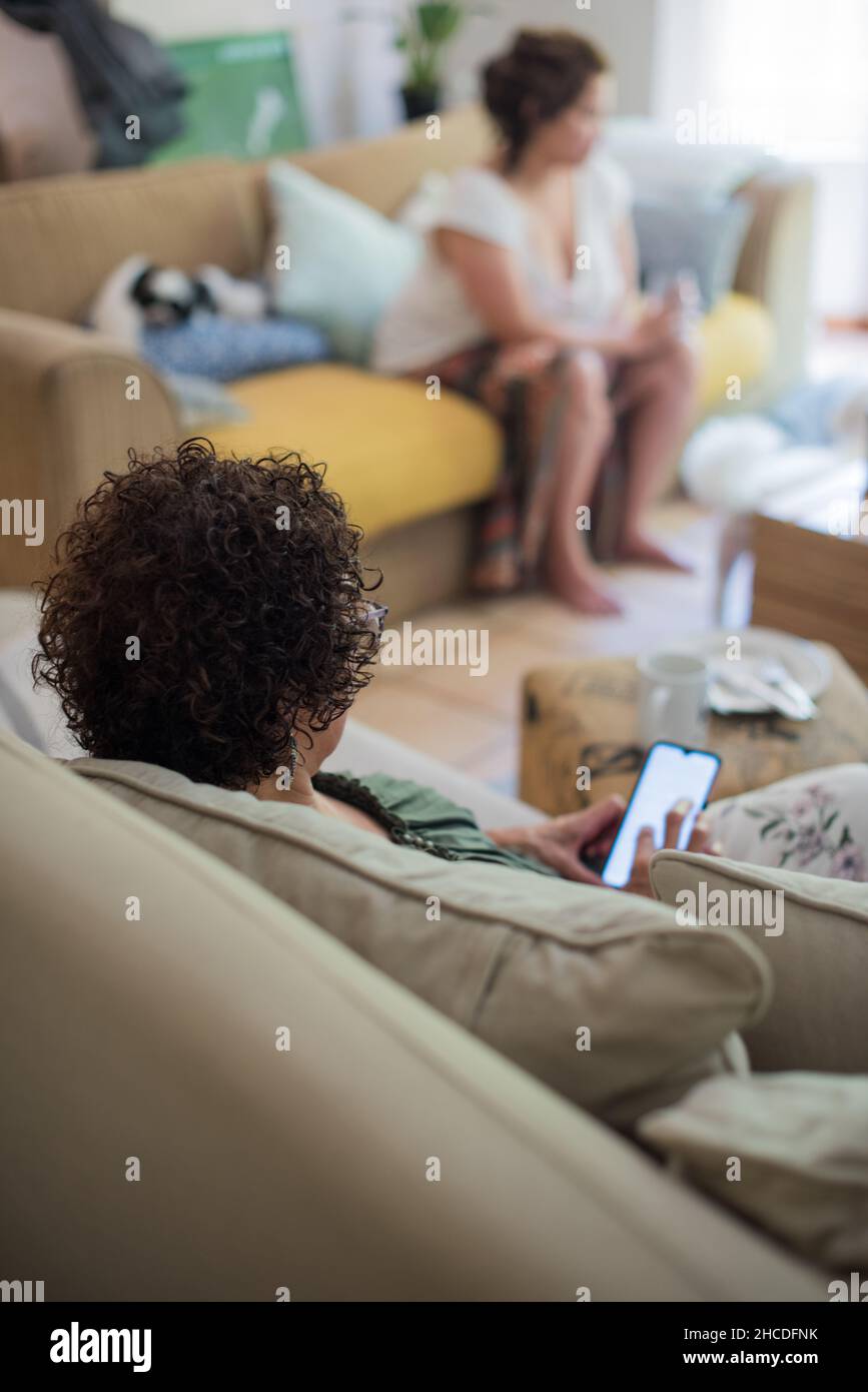 Frau, die ihr Mobiltelefon mit verschwommener Person im Hintergrund benutzt Stockfoto
