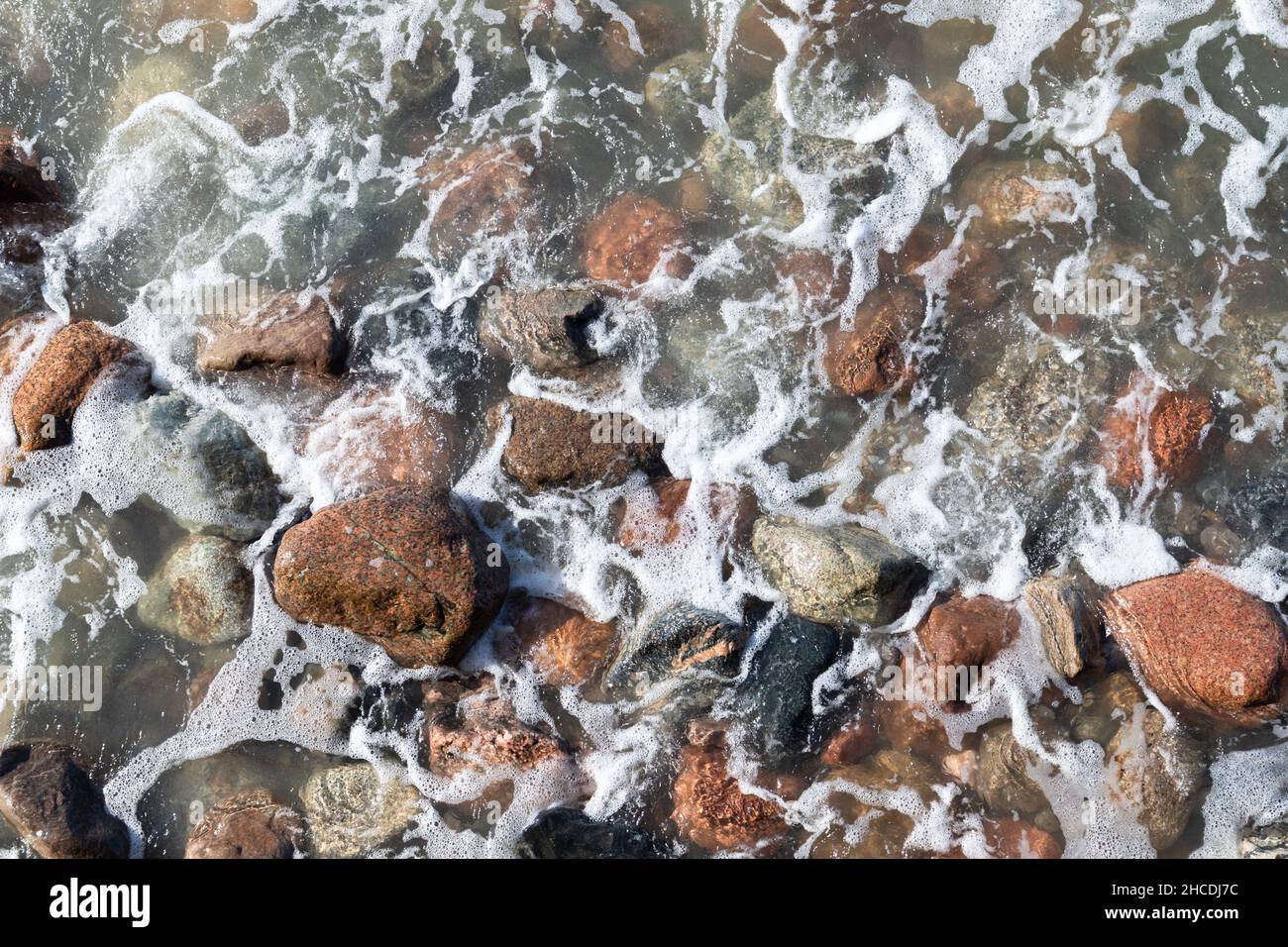 Meerwasser mit nassen Steinen und Schaum. Natürliches Hintergrundbild, Draufsicht Stockfoto