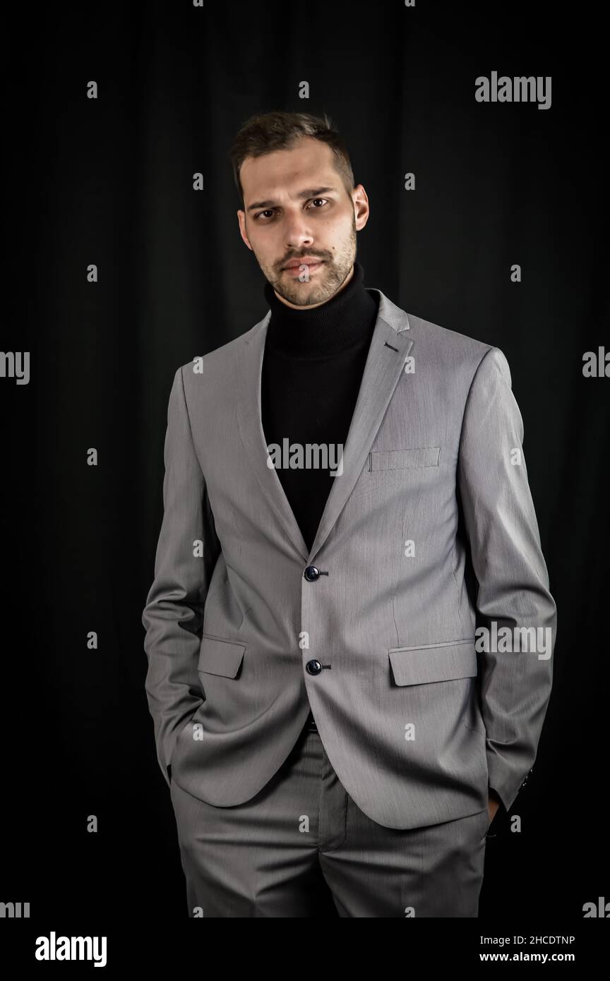 Porträt eines jungen Geschäftsmannes in grauem Anzug und schwarzem Rollkragen, der mit den Händen in den Taschen ernst aussieht Stockfoto