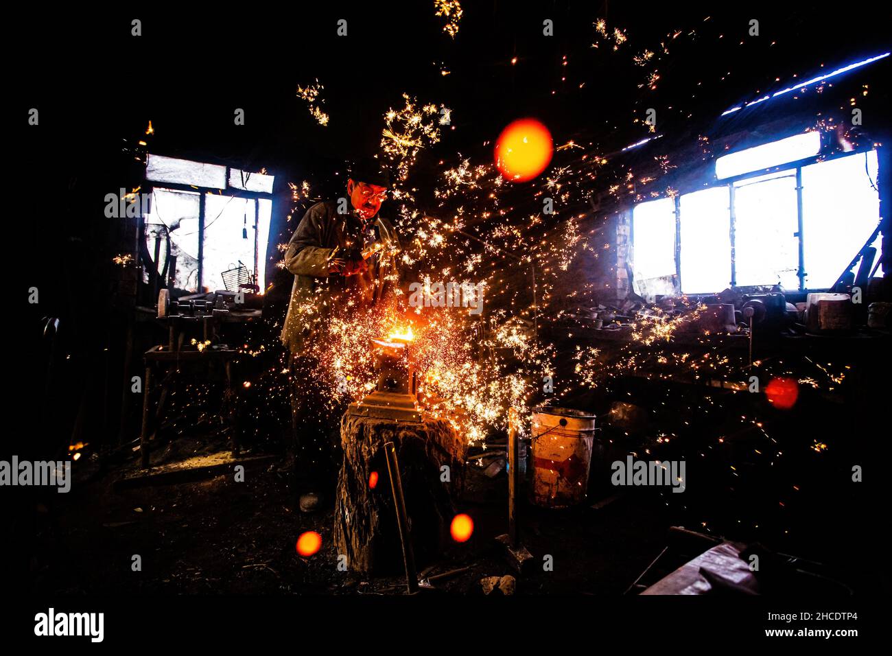 Schmied klopfend und spritzt, mit einem Hammer, heiße Metallteile wie Funken. Das Foto wurde am 17th. April 2021 in der Nähe der Stadt Faget, Landkreis Timis, Banat, aufgenommen Stockfoto