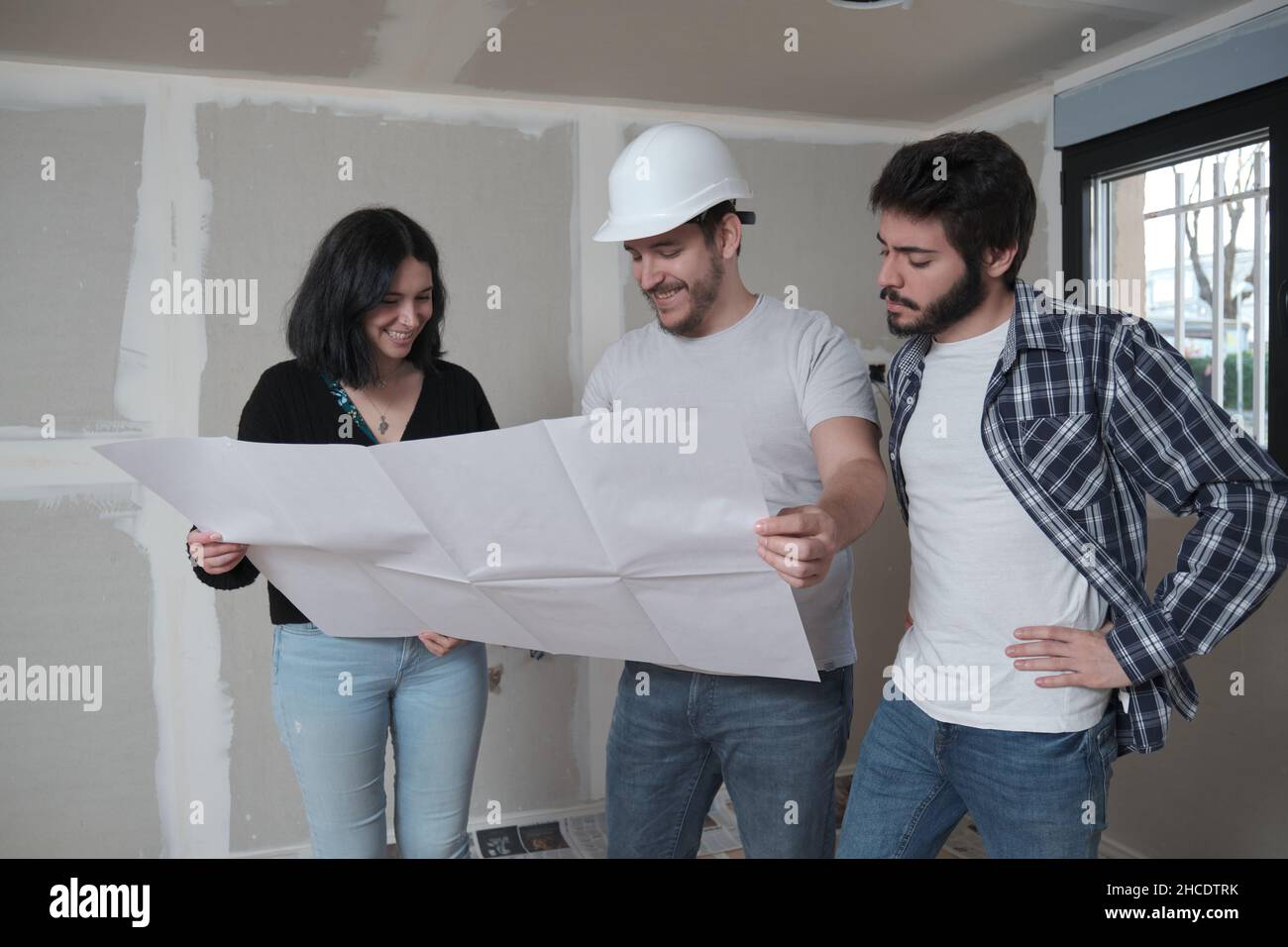 Architekt zeigt dem interessierten jungen Paar Baupläne für eine Wohnung. Stockfoto