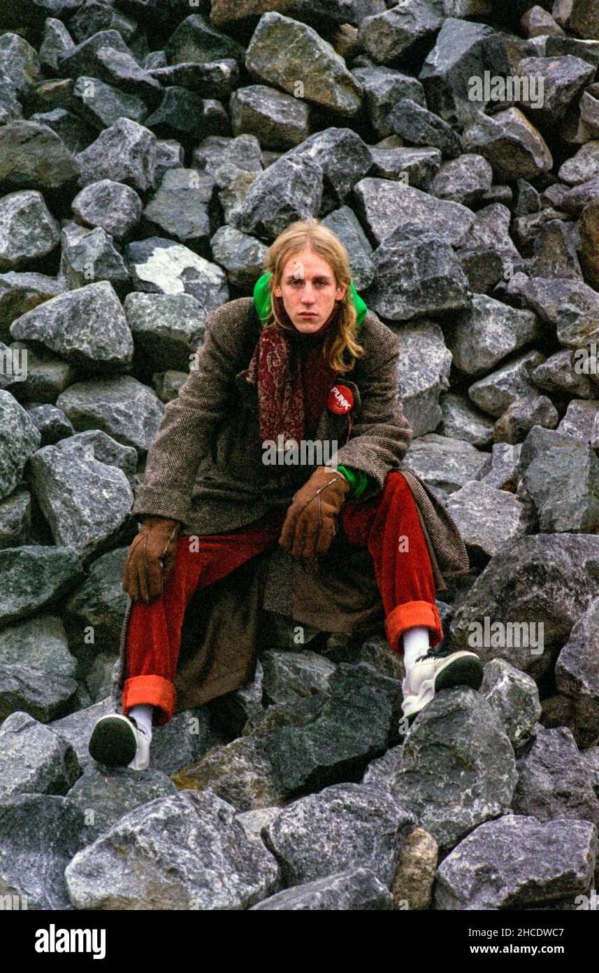 Berlin, Deutschland. Porträt eines jungen Erwachsenen, kaukasischen Musikers und Musikproduzentin , benannt: Leonard Wellington, sitzend auf einem Haufen von Felsen und Steinen in einem Graffiti-Platz. Stockfoto