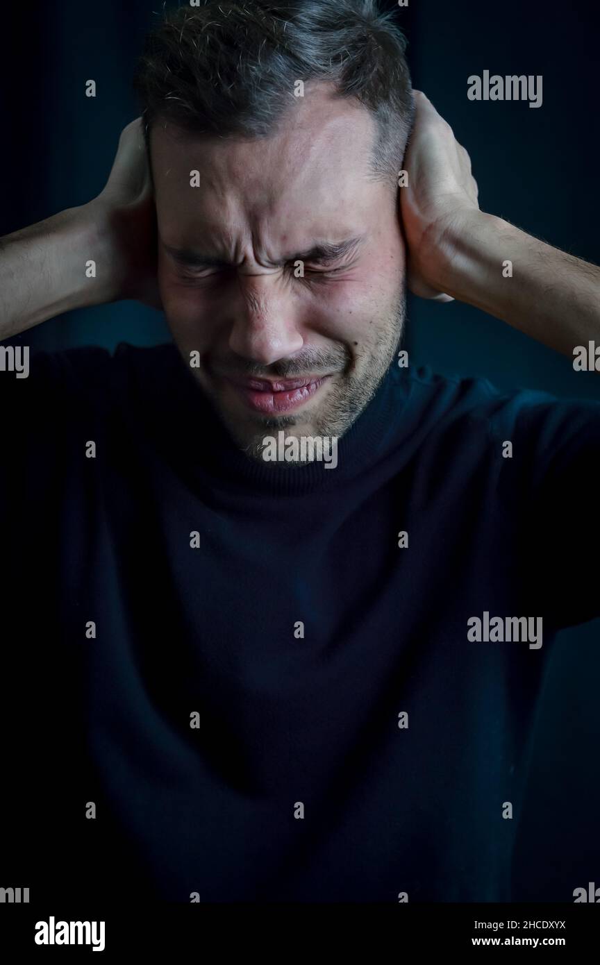 Porträt eines jungen Mannes mit den Händen, die die Ohren bedecken, um nicht zu hören, und geschlossenen Augen, gestört durch den Lärm Stockfoto