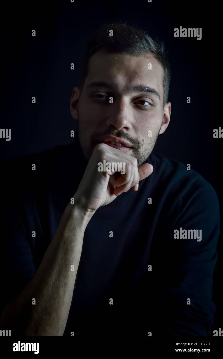 Porträt eines jungen Mannes, dessen Hand auf seinem Kinn liegt und der nachdenklich wegschaut Stockfoto