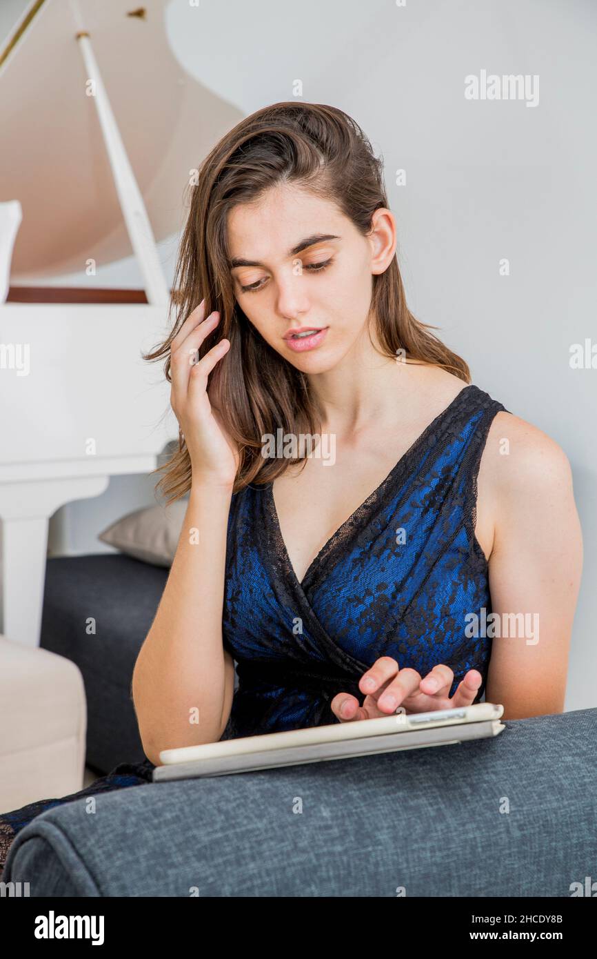 Junge Frau in formeller Kleidung arbeitet zu Hause auf ihrem Tablet, während sie auf einem Mobiltelefon spricht Stockfoto