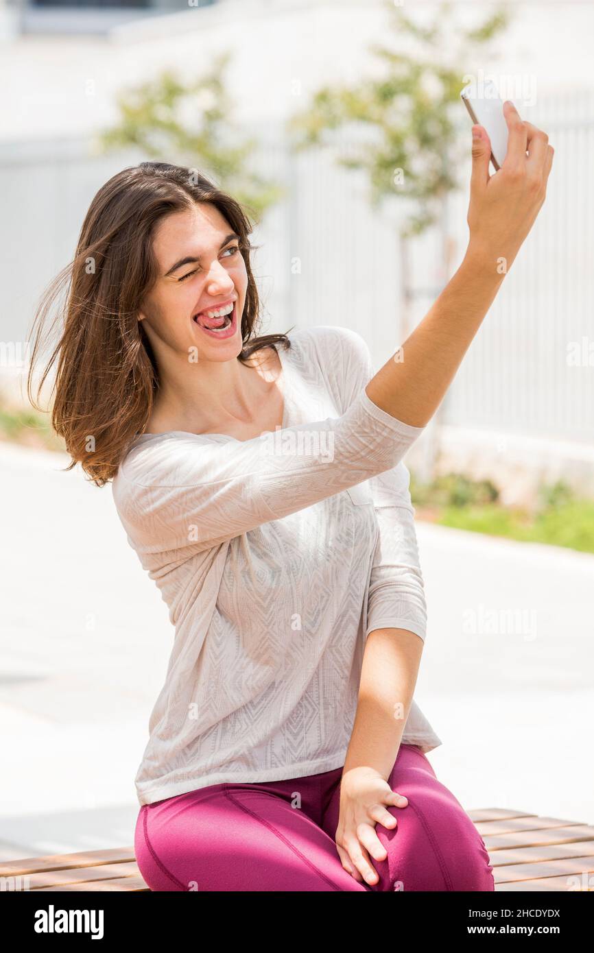 Eine junge Frau in legerer Sportkleidung macht ein Selfie, während sie ihr Gesicht zieht Stockfoto