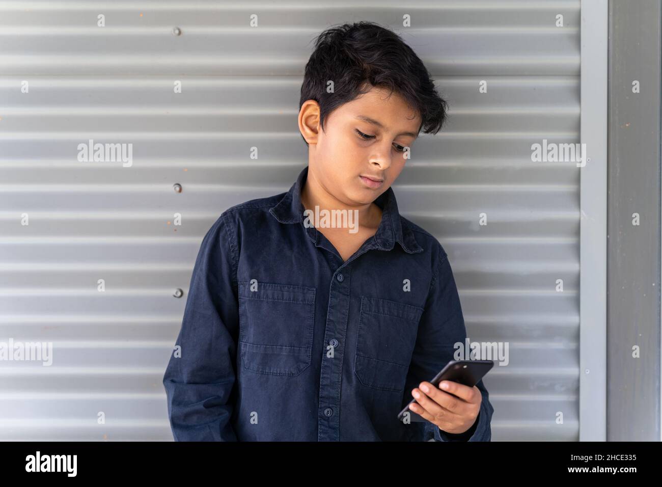 Kleiner Junge, der mit dem Mobiltelefon beschäftigt ist. Konzept eines jungen Kindes, das Social Media auf seinem Handy nutzt. Stockfoto