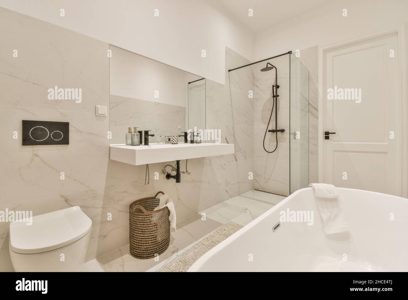 Einrichtung eines modernen weißen Badezimmers mit gefliesten Wänden im Marmordesign, mit einer runden Badewanne gegenüber einer Toilettenschüssel, einem Waschbecken und einer Dusche Stockfoto