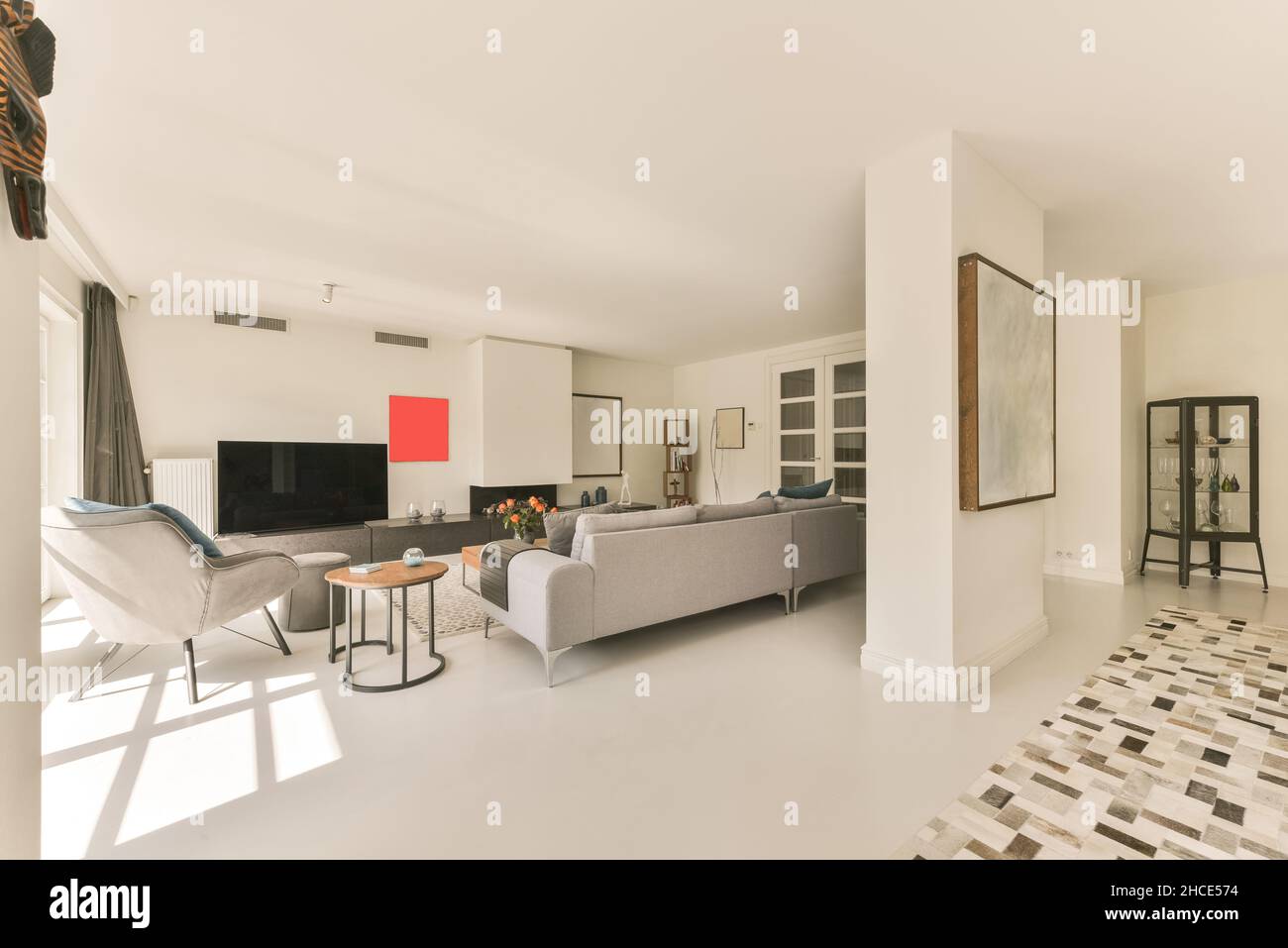 Bequemes graues Sofa und Sessel in einem geräumigen, hellen Wohnzimmer vor dem Fernseher in einer modernen Wohnung an sonnigen Tagen Stockfoto