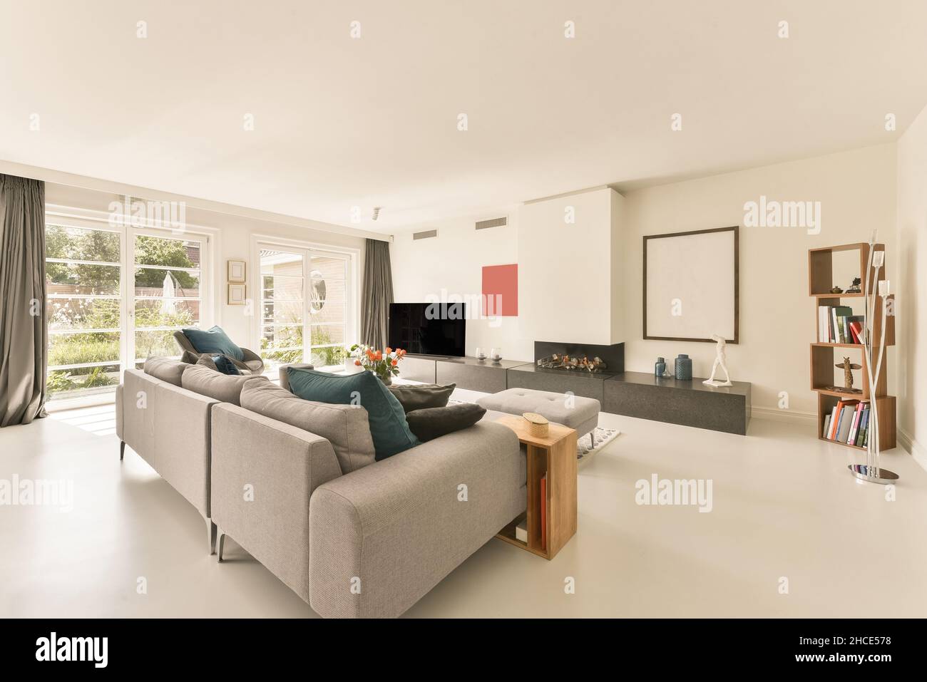 Bequemes graues Sofa und Sessel in einem geräumigen, hellen Wohnzimmer vor dem Fernseher in einer modernen Wohnung an sonnigen Tagen Stockfoto