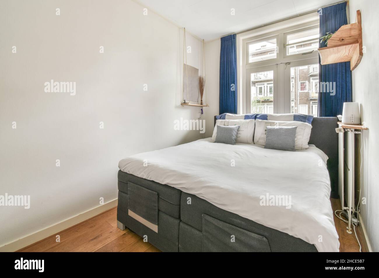 Einrichtung eines modernen Schlafzimmers mit weißen Wänden und einem Bett mit Kissen auf der Decke, das an sonnigen Tagen in der Nähe des Fensters aufgestellt wurde Stockfoto