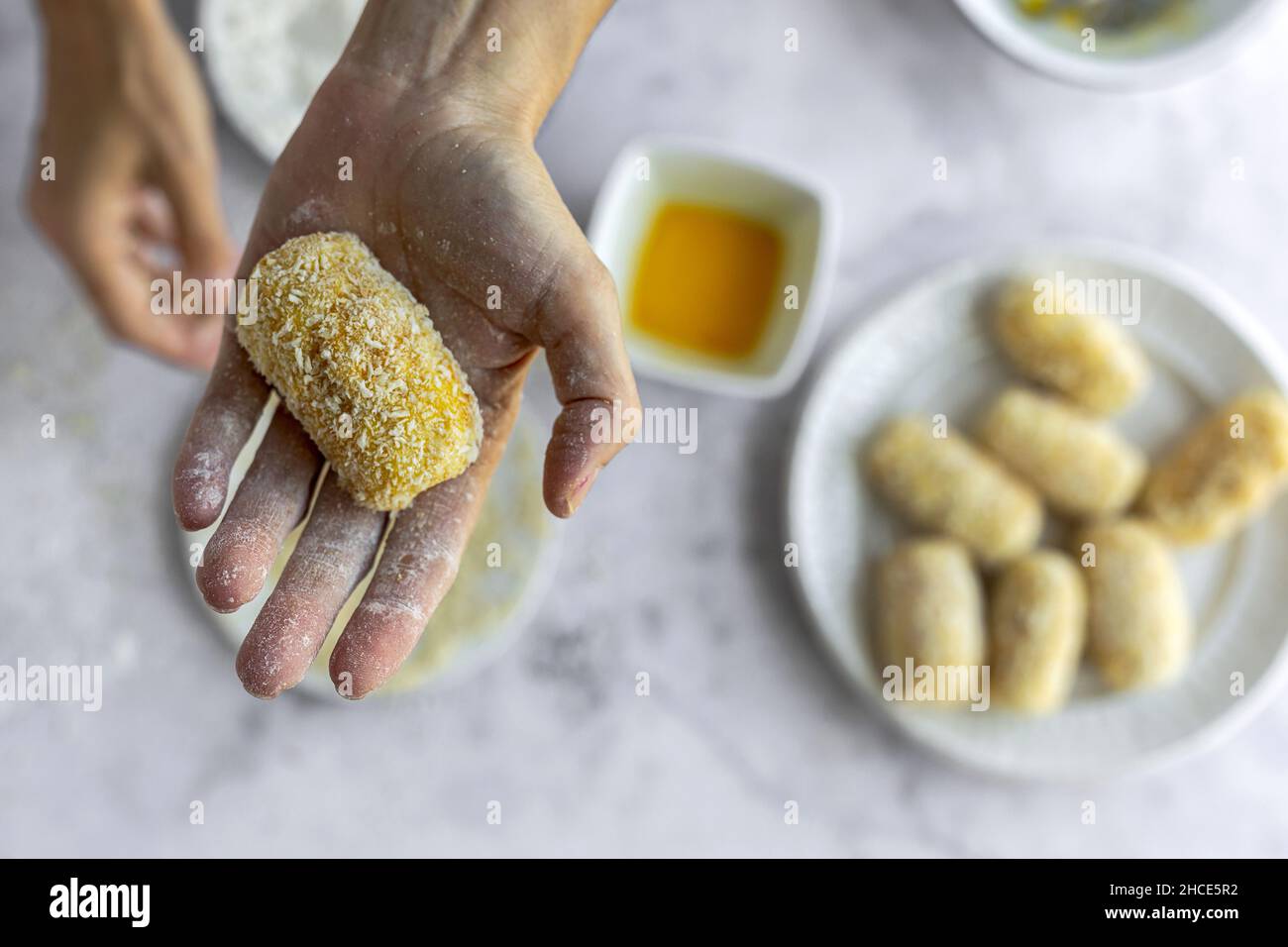 Draufsicht weicher Fokus der Ernte unkenntlich Koch zeigt leckere rohe Kartoffelcroquette mit Paniermehl überzogen beim Kochen am Tisch in der Küche Stockfoto