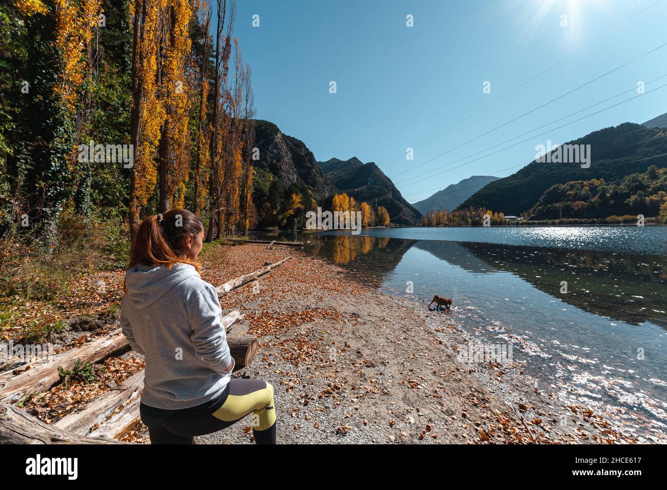 Rückansicht der nicht erkennbaren weiblichen Touristen, die am Ufer des Flusses auf einem Baumschnäpfel stehen und die atemberaubende Landschaft mit ruhigem Wasser und Bergen von Torrass genießen Stockfoto