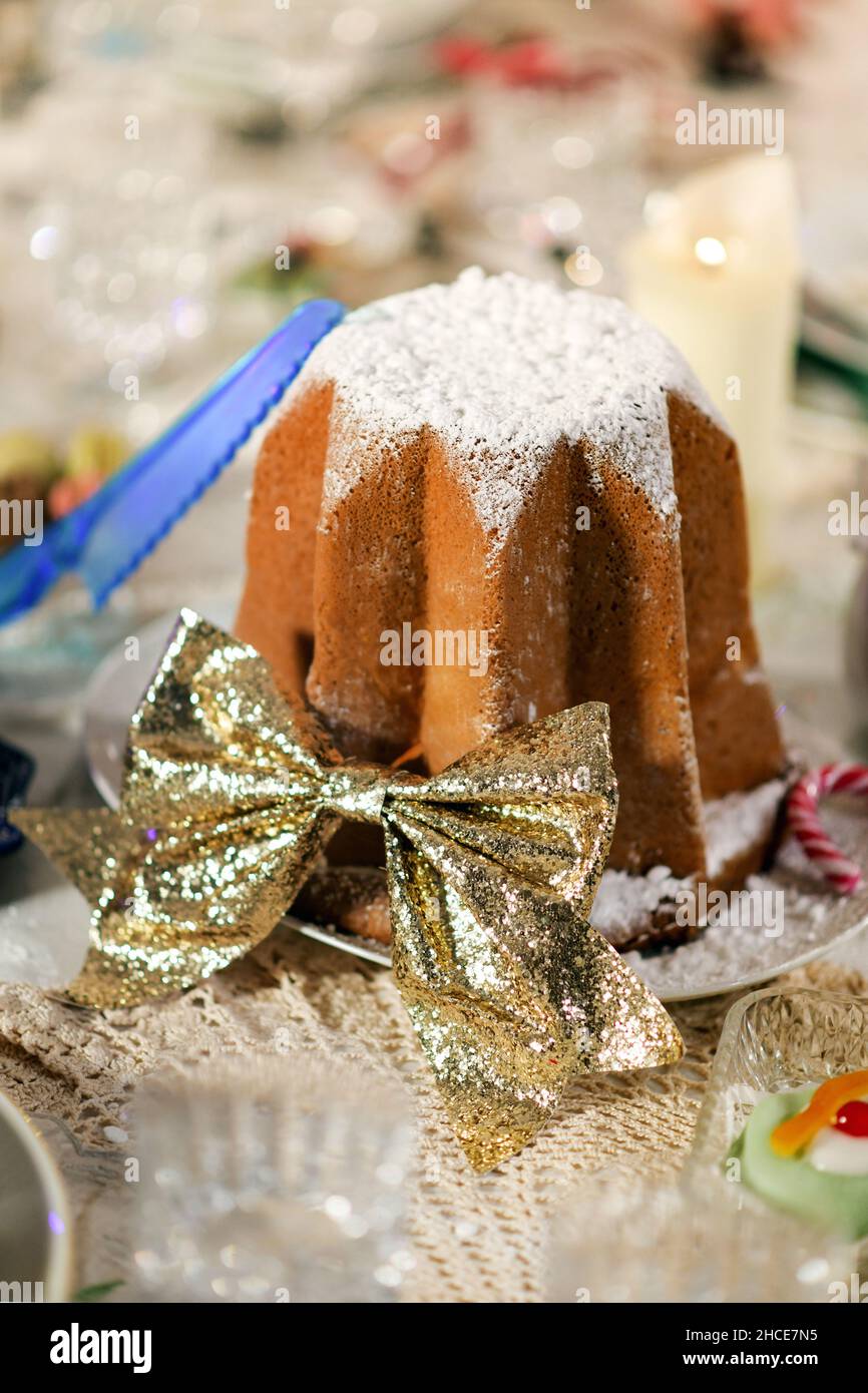 Hoher Winkel von traditionellen italienischen Pandoro Dessert mit Puderzucker mit goldener Schleife auf dem Tisch zum Weihnachtsessen dekoriert Stockfoto