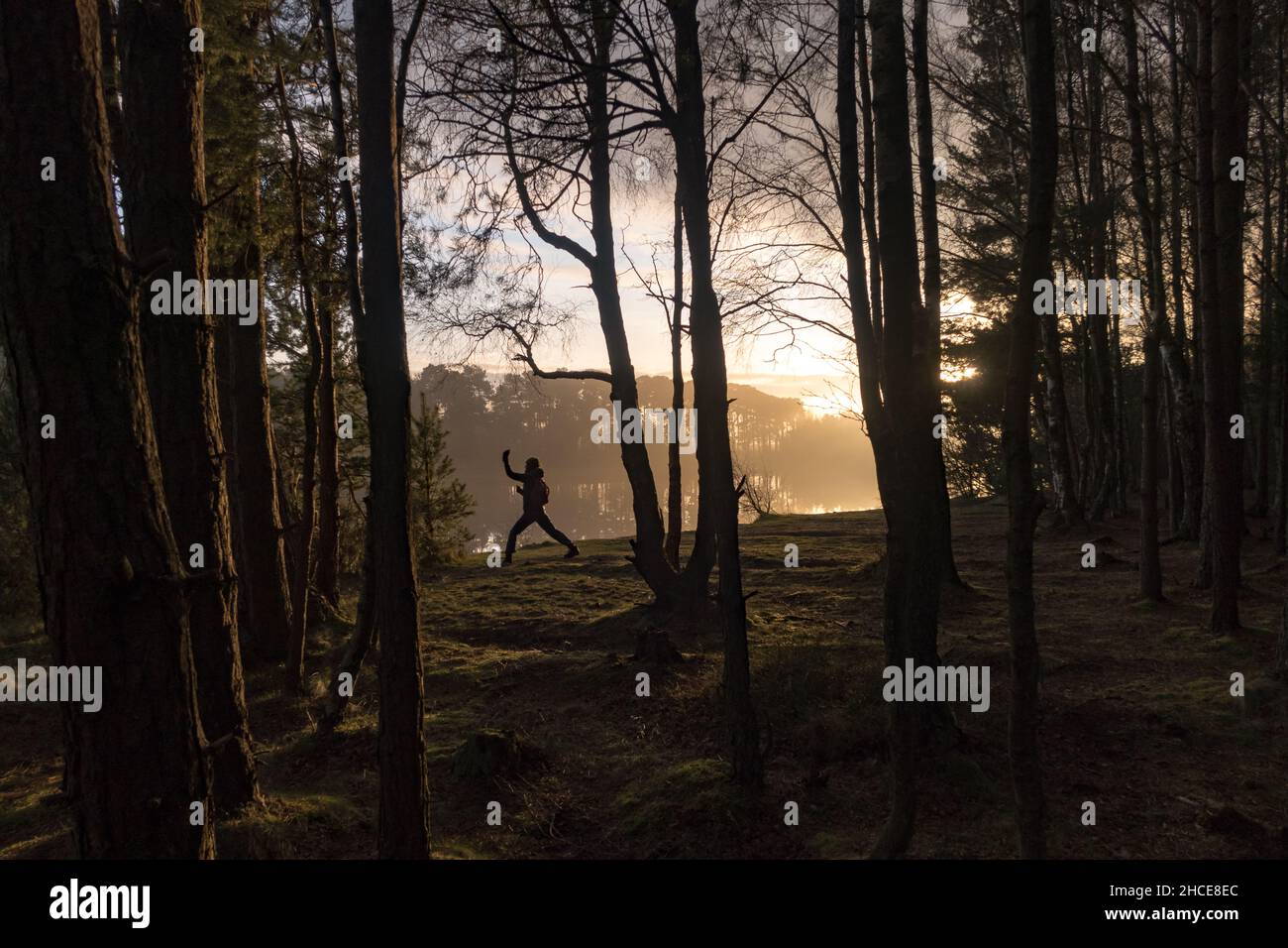 Eine Person, die im Winter in einem Wald am Fluss eines Sees bei Sonnenuntergang Übungen macht Stockfoto