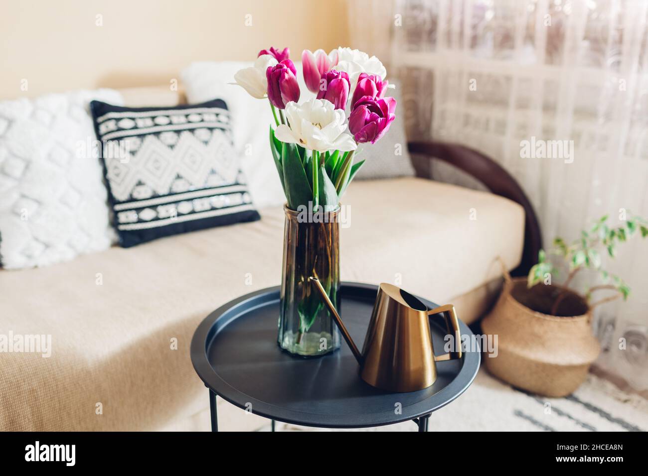 Inneneinrichtung und Inneneinrichtung. Frische Tulpen Blumen in Vasen auf Couchtisch mit goldenen Metall Gießkanne Stockfoto