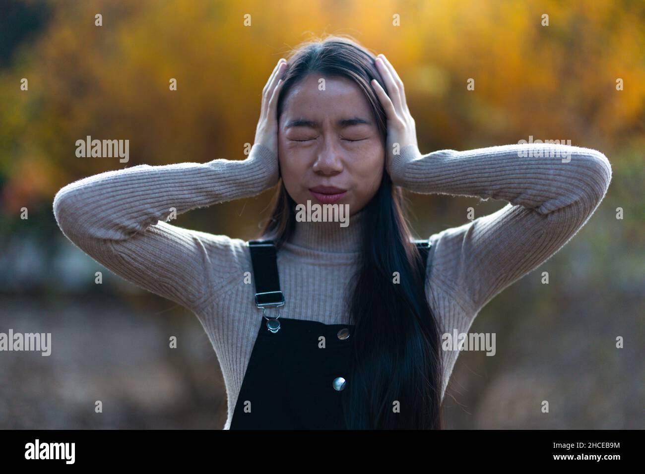 Junges asiatisches Teenager-Mädchen, das ihre Ohren mit den Händen auf der Straße bedeckt Stockfoto