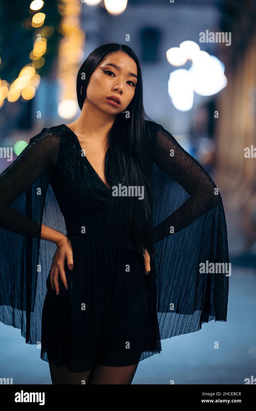 Mode-Porträt der jungen asiatischen Frau mit Händen auf der Taille in der Straße in der Nacht trägt Partykleid Stockfoto