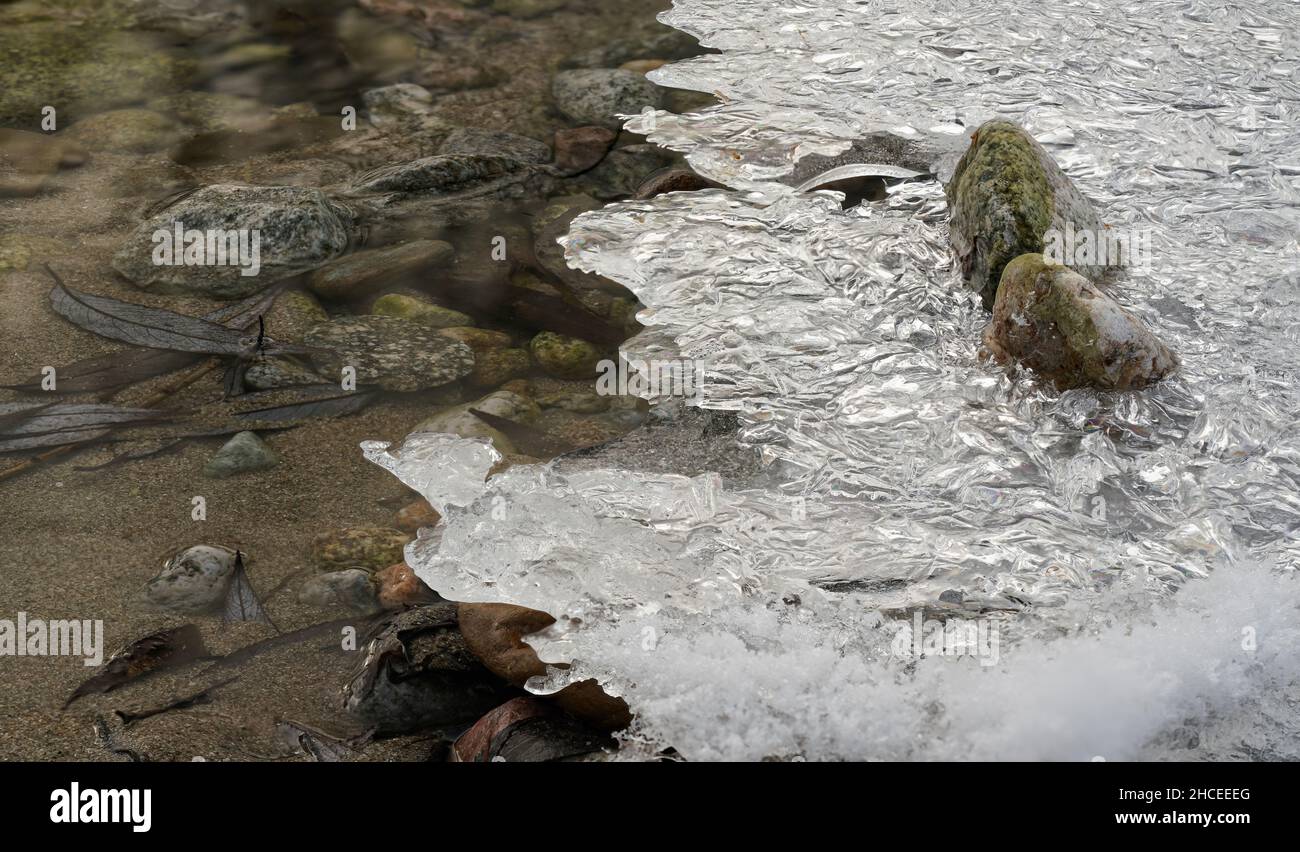 Dünnes Eis bedeckt felsiges Flussufer, Wasser fließt in der Nähe - Nahaufnahme Winter Detail Stockfoto