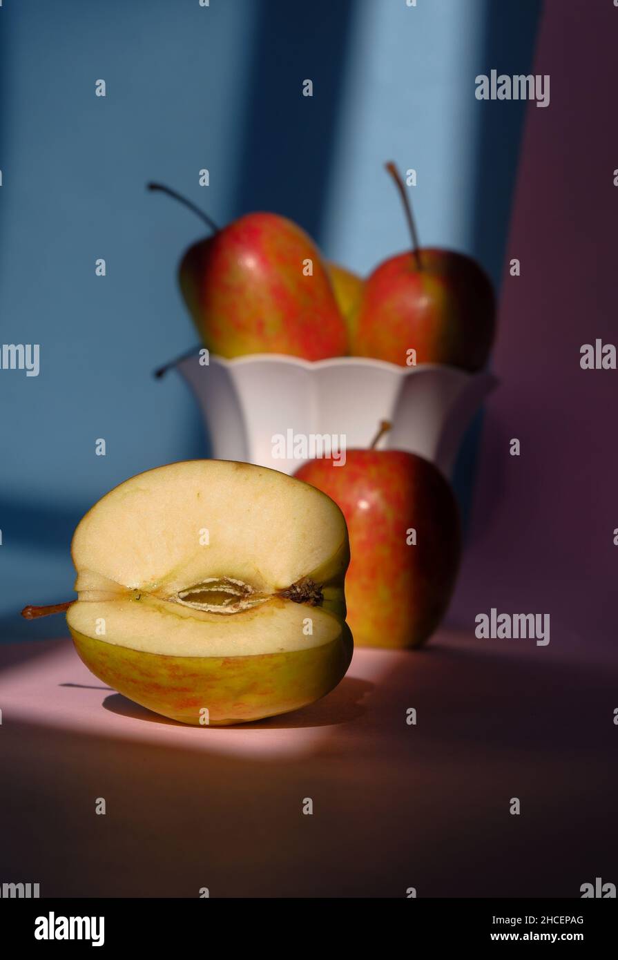 Foto eines Apfels in einem Behälter auf einem rosa und blauen Hintergrund Stockfoto