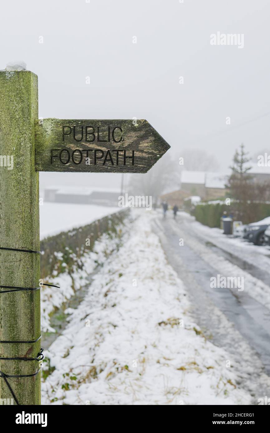 Ein öffentliches Wanderwegschild auf einer Landstraße neben Otley Chevin, Yorkshire, während des Schneefalls im Winter 2021. Stockfoto