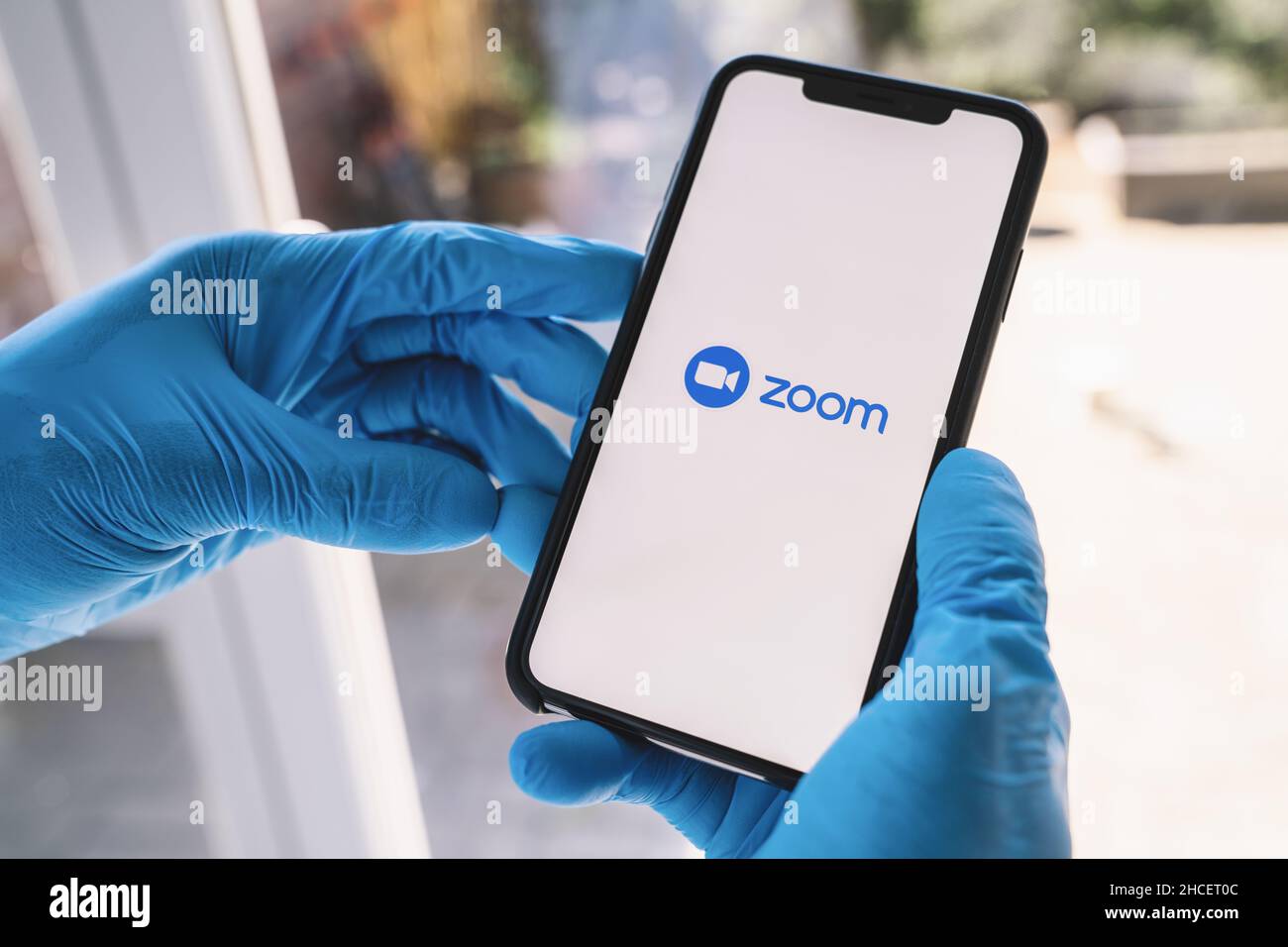 Mann mit Handschuhen, der die Zoom Mobile App auf ihrem Smartphone öffnet. Zoom-Benutzer können Sitzungen aufzeichnen, an Projekten zusammenarbeiten und freigeben oder kommentieren Stockfoto