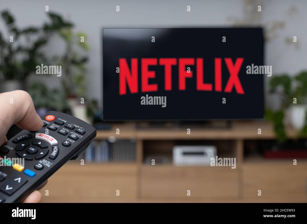 TV-Fernbedienung in der Hand und Netflix-Logo im Hintergrund. Netflix ist ​​the globale Anbieter von Streaming-Filmen und TV-Serien. Stockfoto