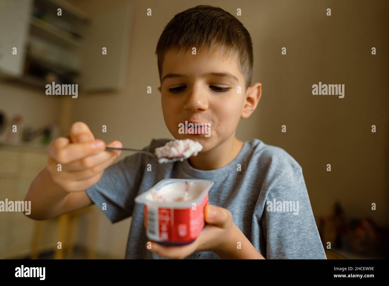 Süßer Junge mit Appetit isst Joghurt mit Löffel, Grimassen. Stockfoto