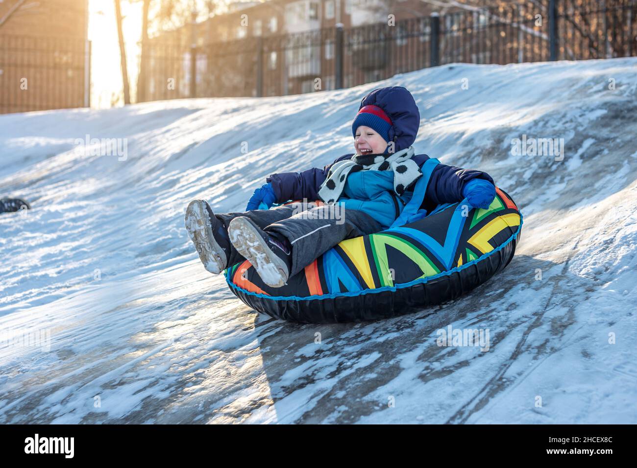 Ein glückliches Kind mit seiner Mutter schlaucht mit einem Park von einer Rutsche. Ein lustiges Winterwochenende im Park draußen. Stockfoto