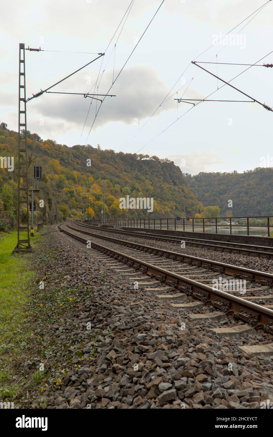Vertikale Aufnahme von Eisenbahnschienen und Stromleitungen, die nach links mit Blick auf den Bergwald fahren Stockfoto