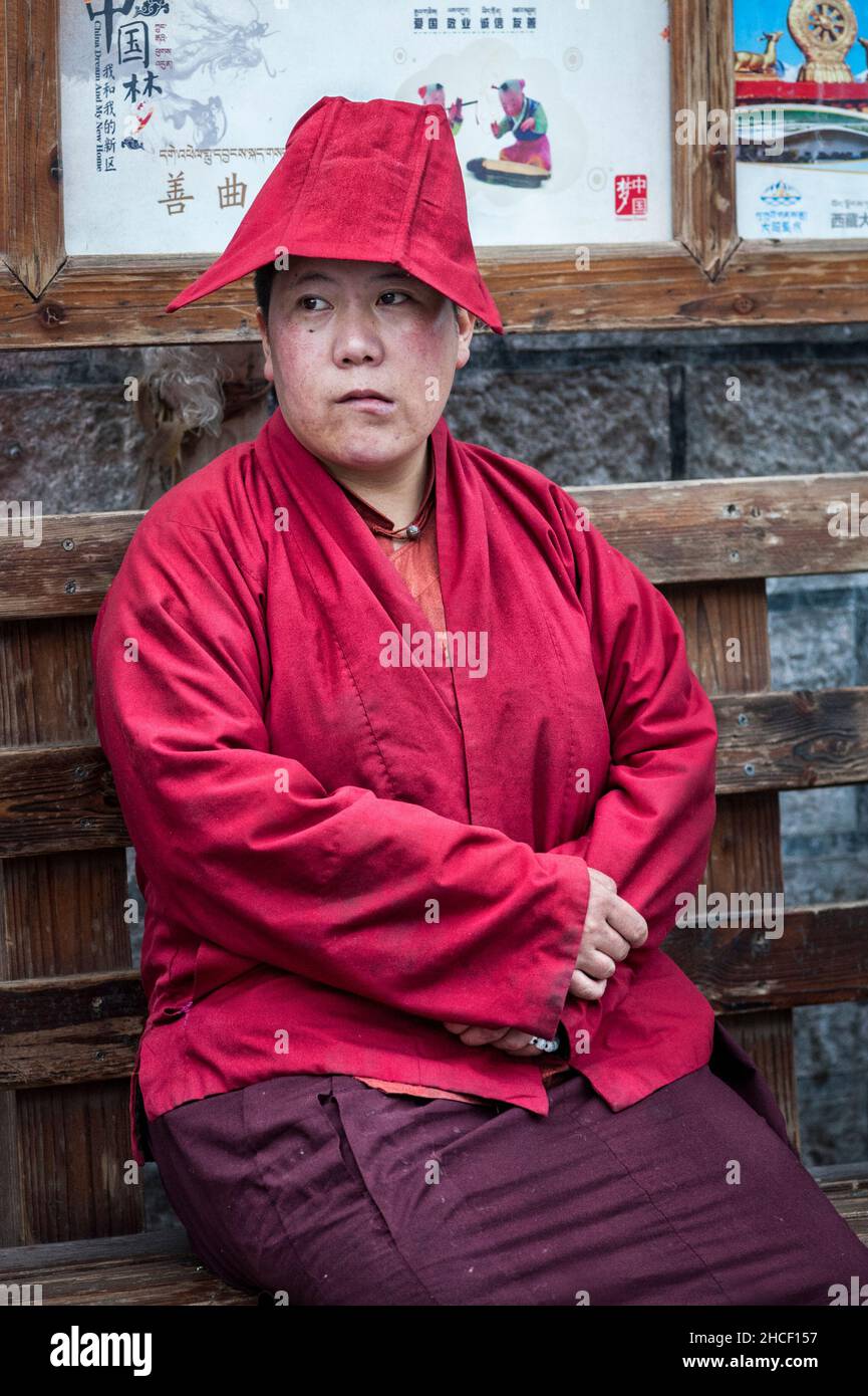 A, TIBET, CHINA - AUGUST 17 2018: Nicht identifizierter Tibeter in traditioneller Kleidung sitzt auf einer Bank in der Nähe des Jokhang-Tempels Stockfoto