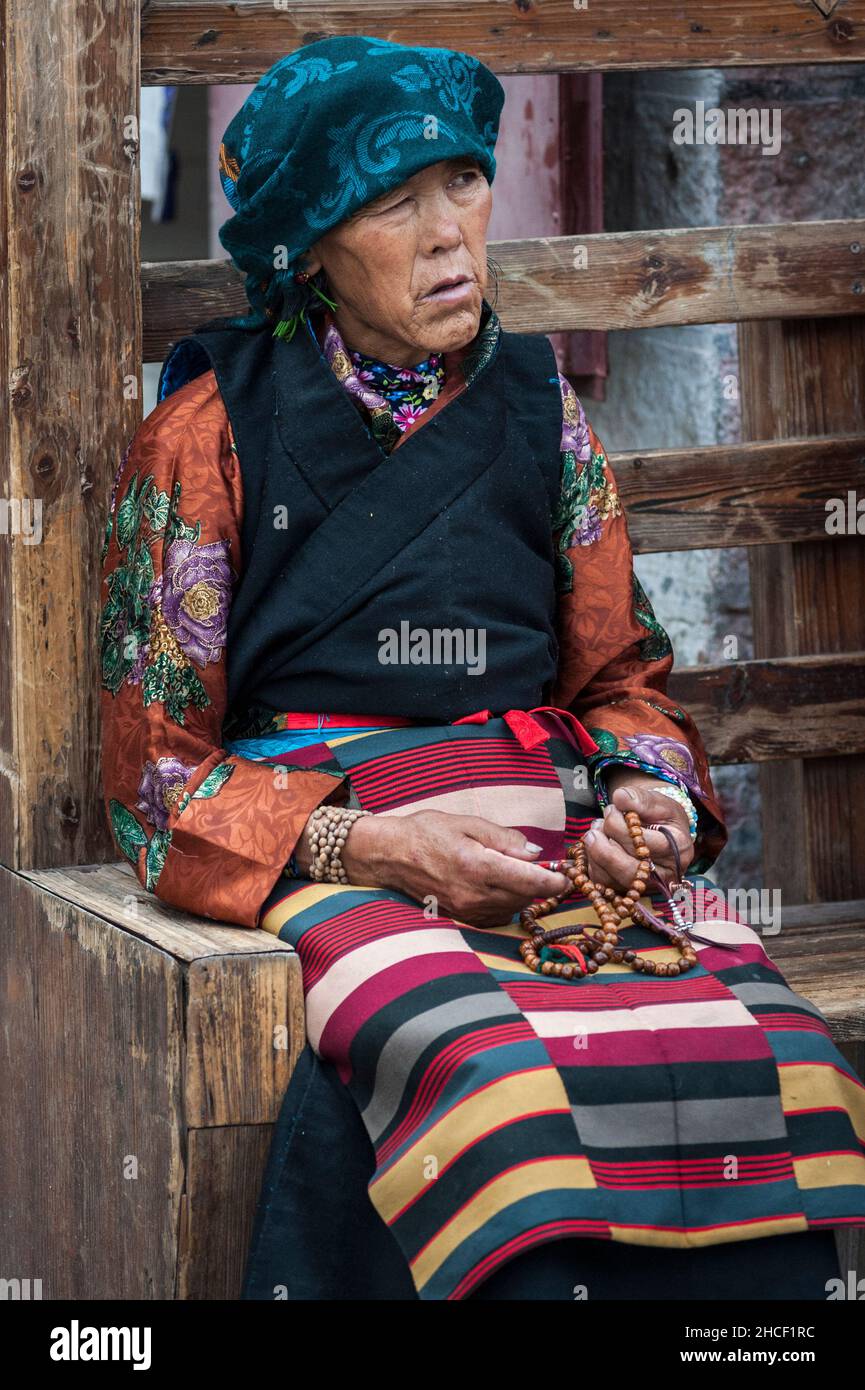 Eine alte tibeterin in traditioneller Kleidung sitzt auf einer Bank in der Nähe des Jokhang-Tempels Stockfoto