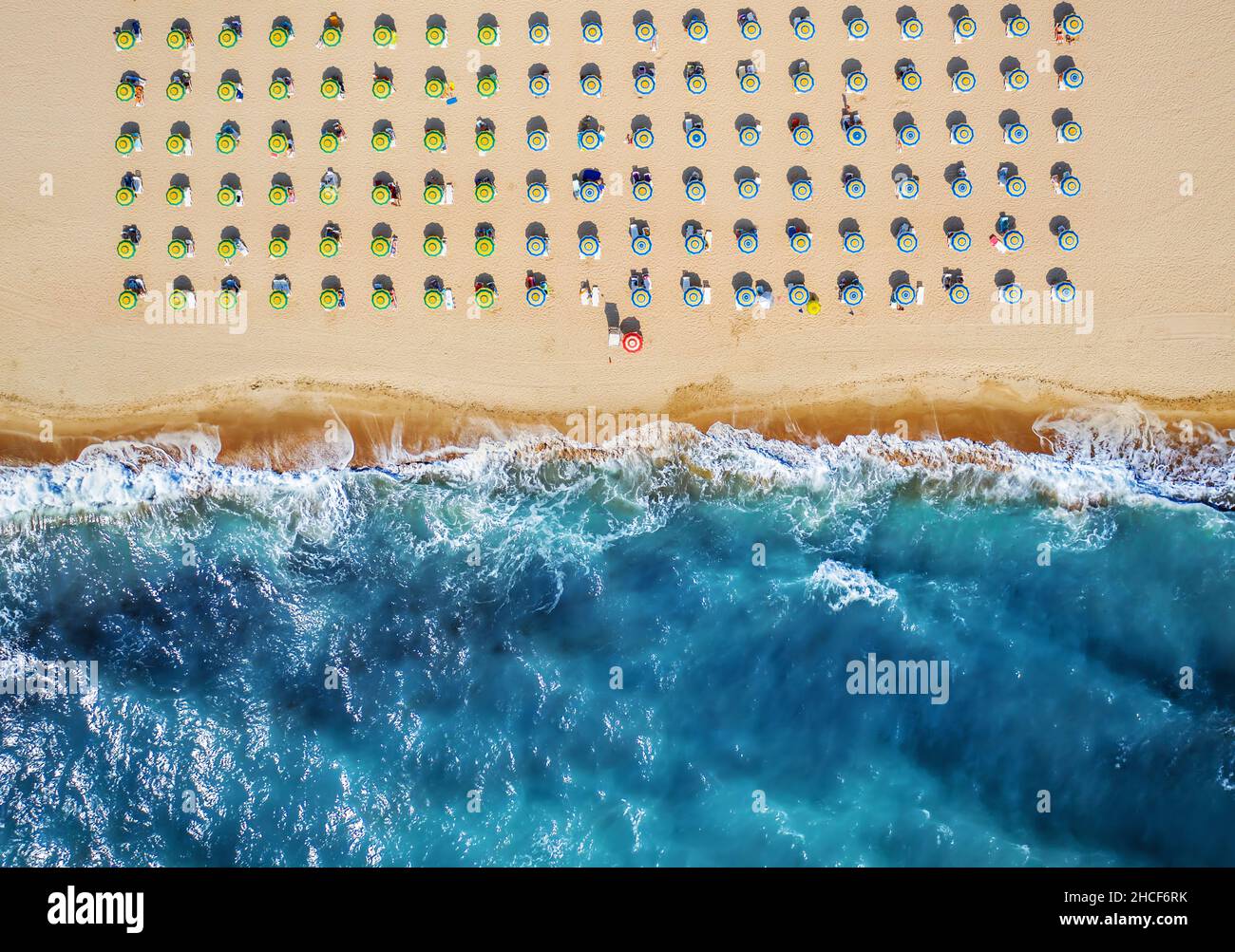 Blick von oben auf den Strand mit Strohschirmen. Regenschirme, Sand- und Meereswellen-Landschaft. Stockfoto