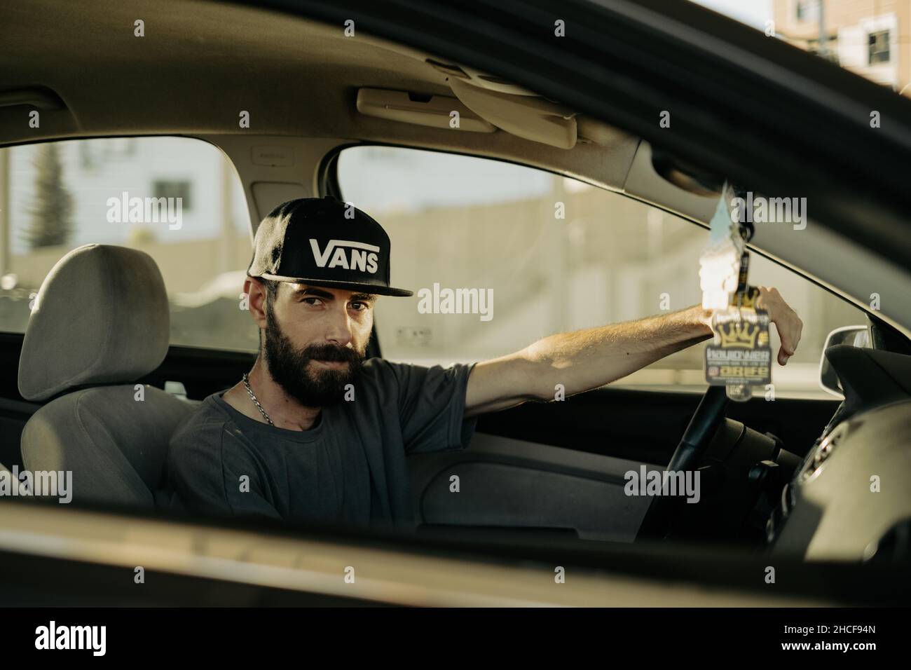 Mann, der selbstbewusst im Auto posiert und Vans Baseballmütze trägt Stockfoto
