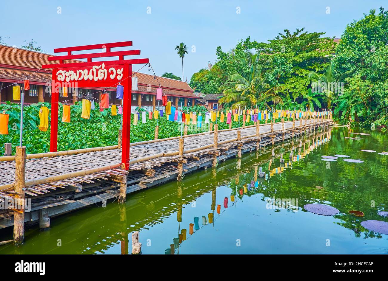 Das rote dekorative Holztor und der Bambussteg auf dem Teich mit Lotusblumen und Seerosen im Park des Wat Chetlin (Jedlin, Jetlin)-Tempels, Chiang Mai, Stockfoto