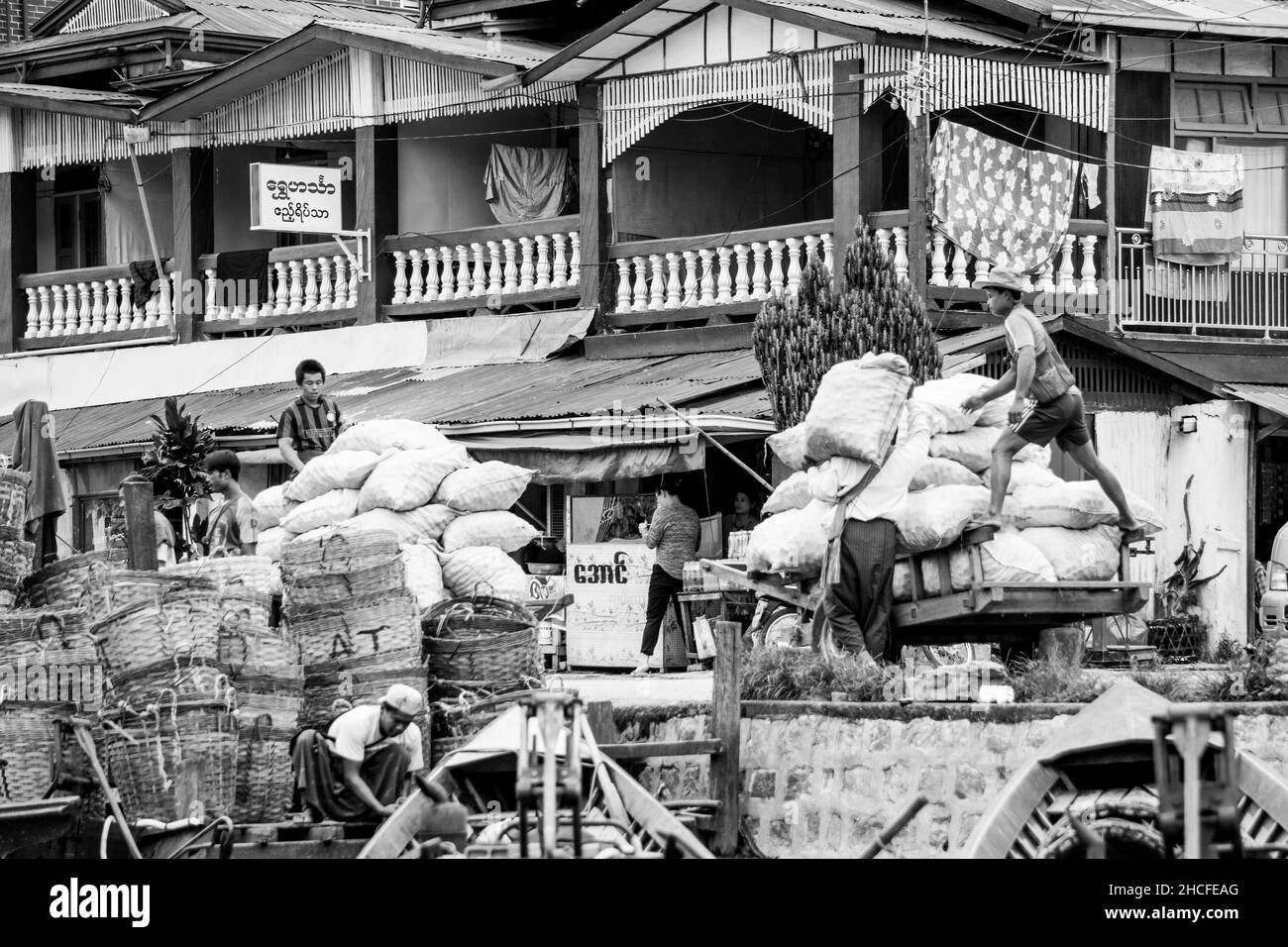 Burmesische Männer laden und entladen Säcke mit Vorräten und Lebensmitteln von Booten zu Karren, in Inle Lake Stockfoto