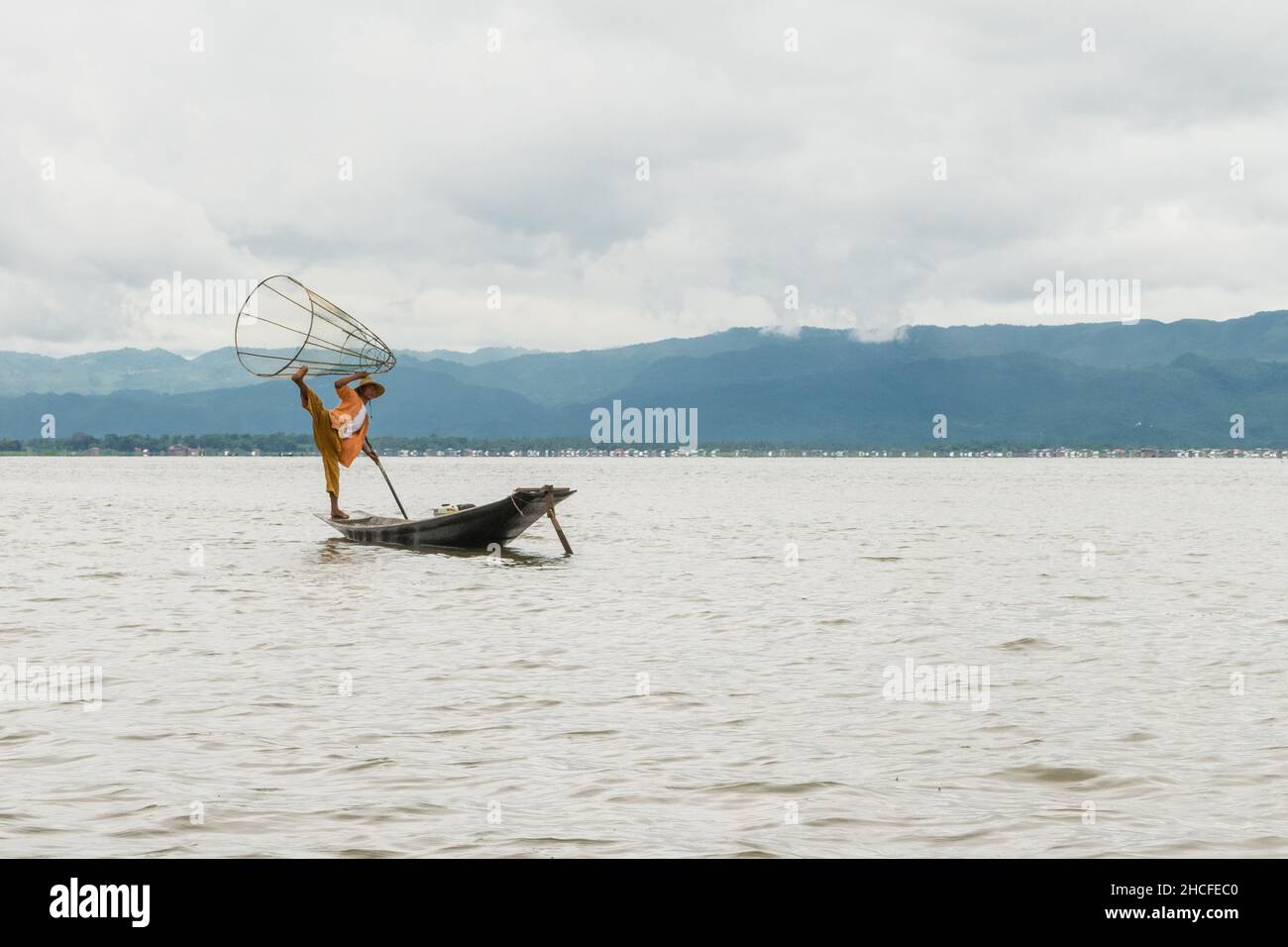 Lokaler birmanischer Fischer posiert mit seinem Netz für Fotos, balanciert und steuert Boot mit einem Fuß. Stockfoto