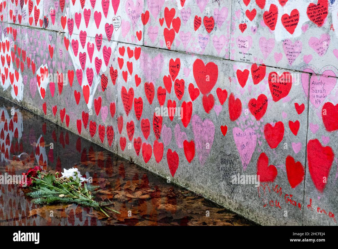 Londons National Covid Memorial Wall mit verfallenden Blumen im Vordergrund. Sowohl die Herzen als auch die Blumen haben sich im Laufe der Zeit verschlechtert. Stockfoto