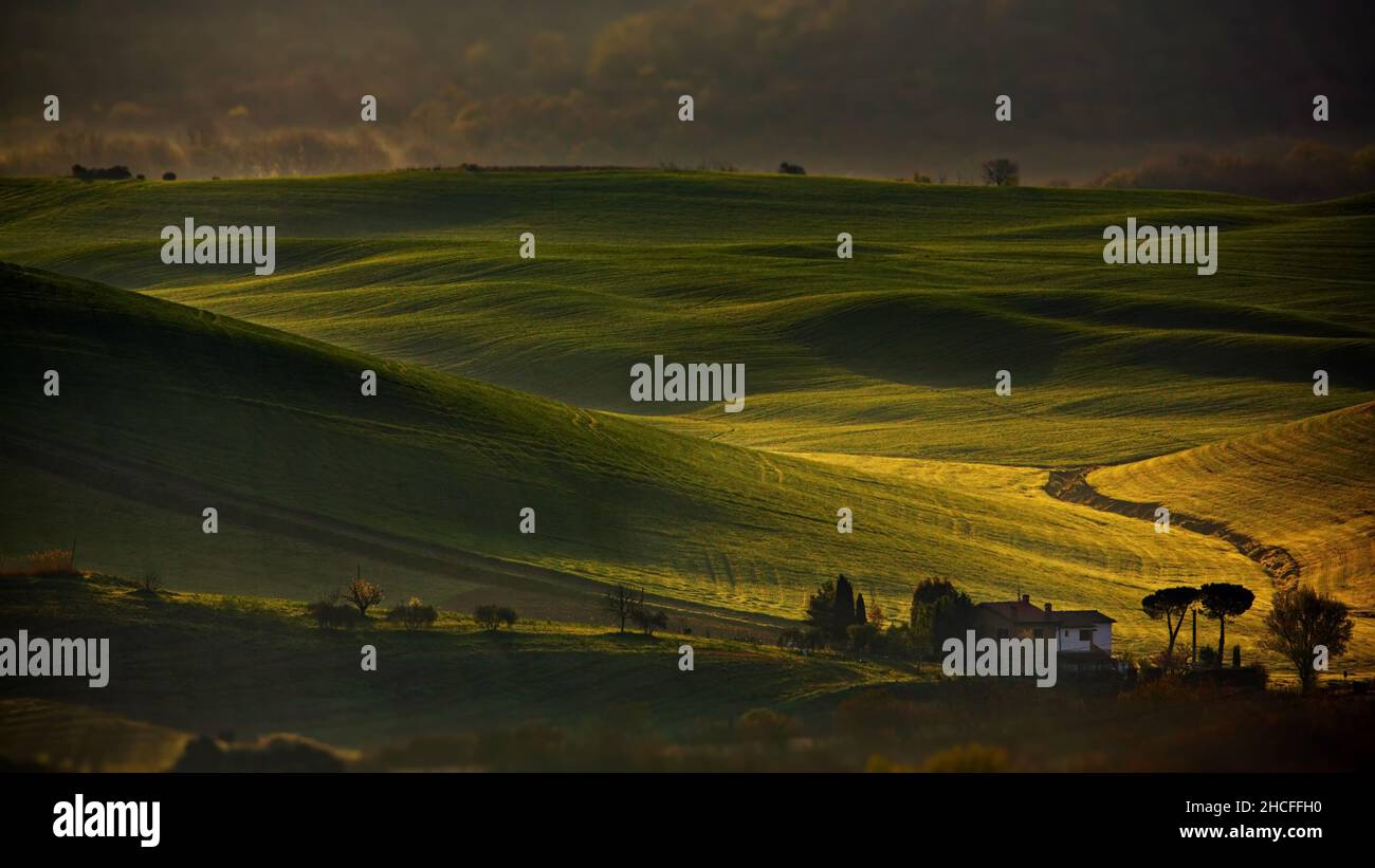 Schöner Panoramablick auf eine grüne Wiese mit einem Landhaus bei Sonnenaufgang in der Toskana, Italien Stockfoto