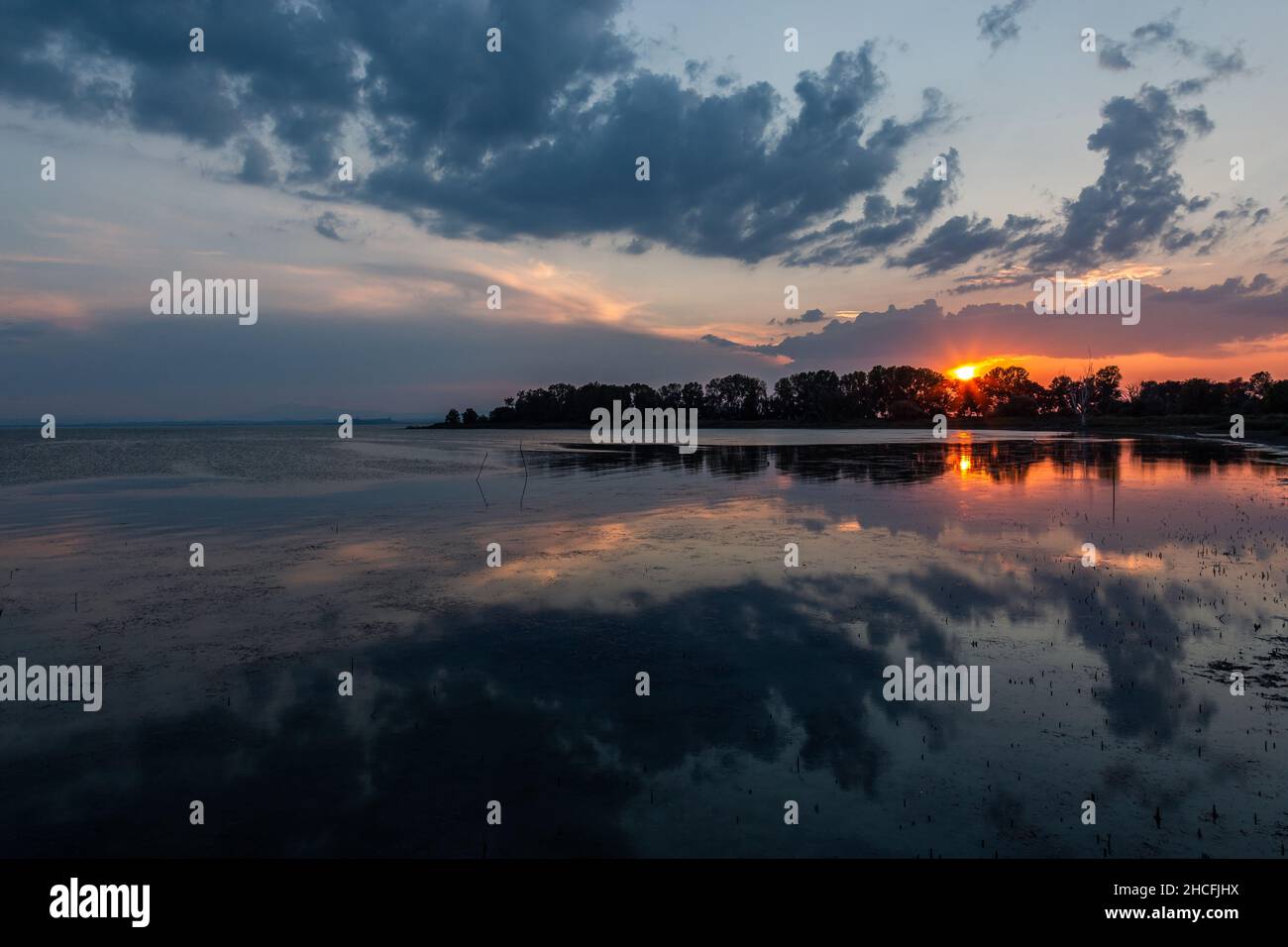 Perfekt symmetrische Wolken und Baumreflexe auf einem See bei Sonnenuntergang Stockfoto