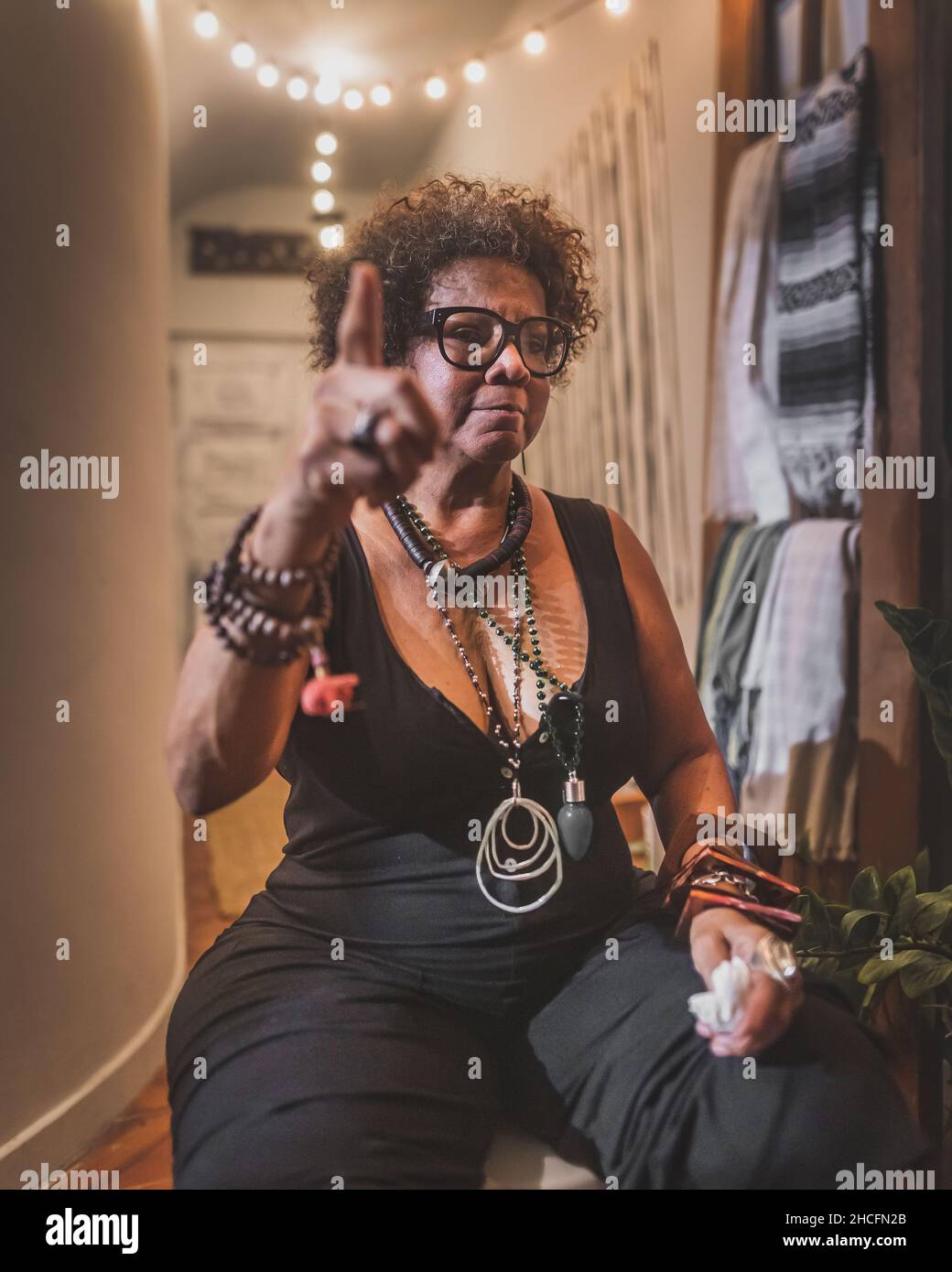 Vertikale Aufnahme einer coolen afroamerikanischen Frau in Schwarz und Schmuck, die auf etwas zeigt Stockfoto